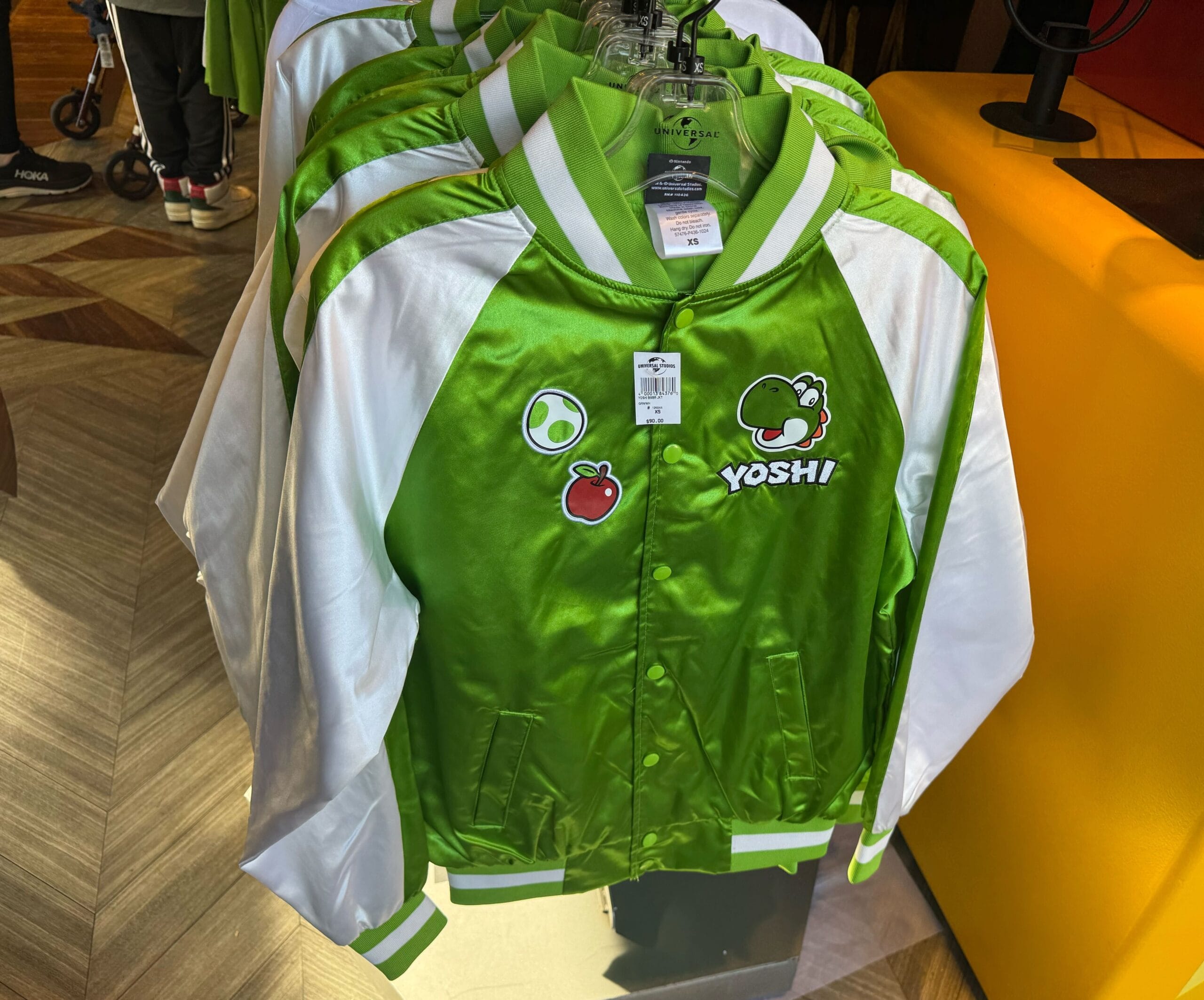 Green and white Yoshi jackets, exclusive Yoshi merchandise, hang on a rack in a store.