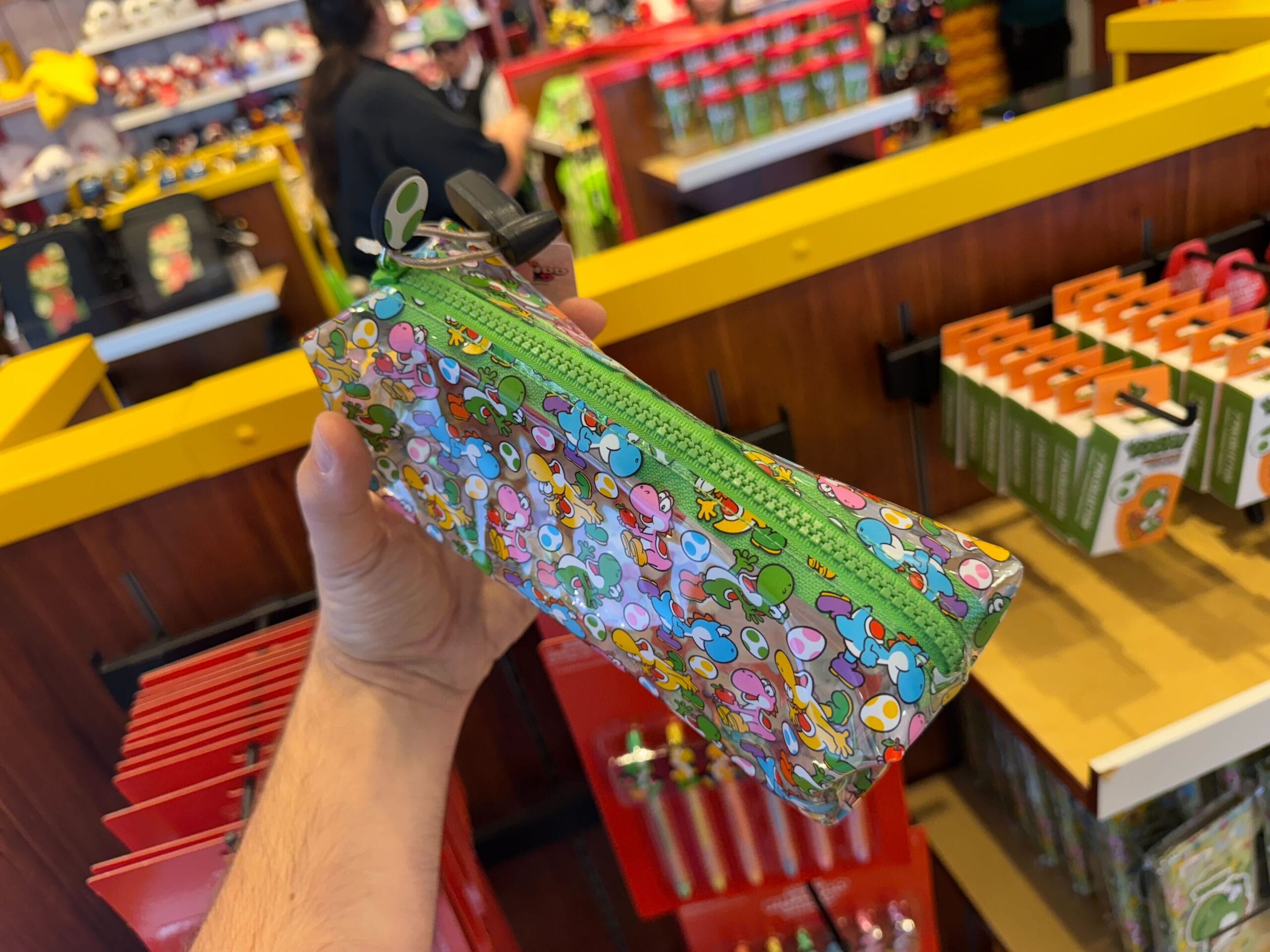A hand holds a green Yoshi merchandise pencil case in a colorful store at Universal Studios Hollywood.