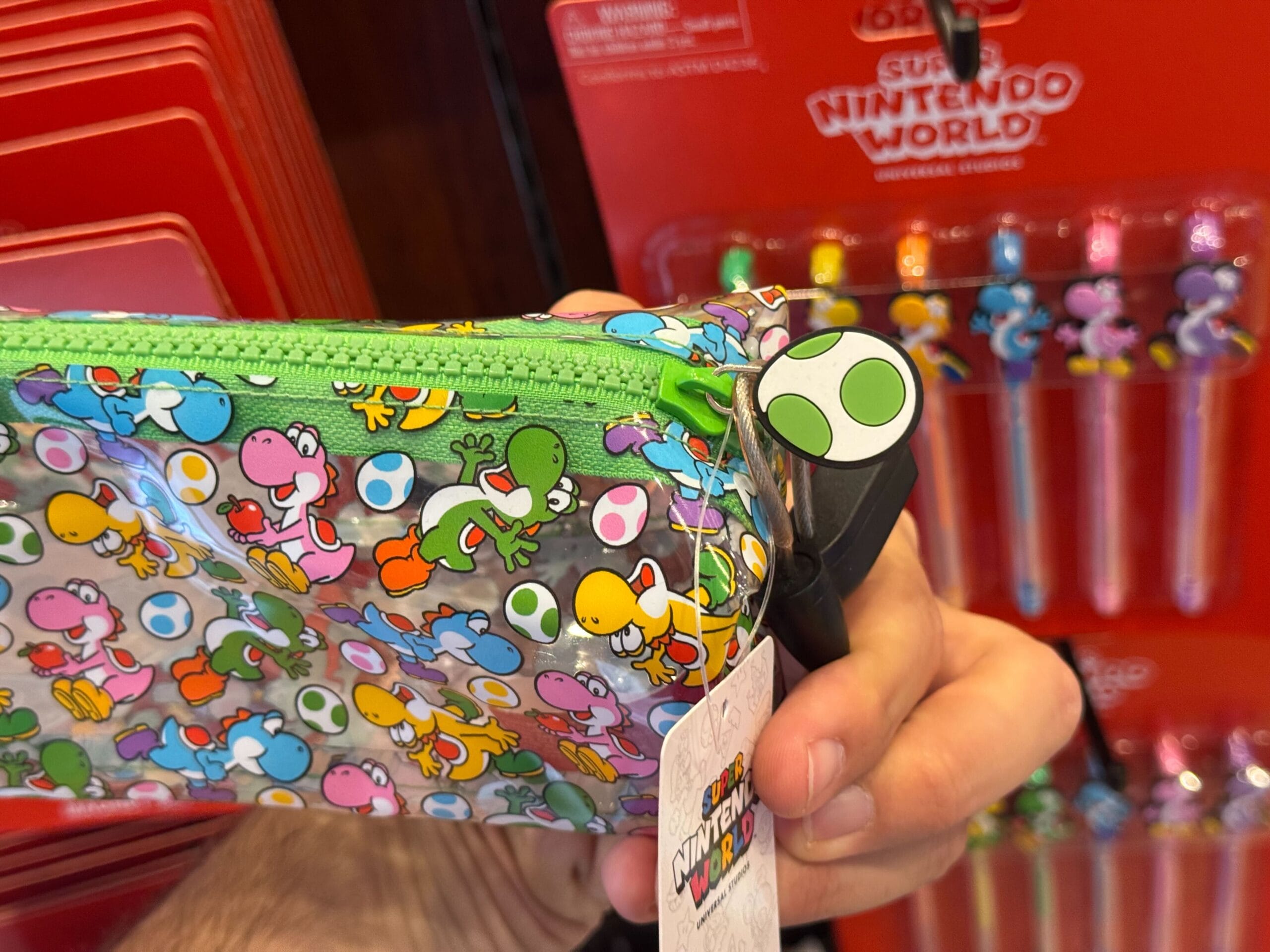 A hand holds Yoshi merchandise at Universal Studios Hollywood; Super Nintendo World pens are in the background.