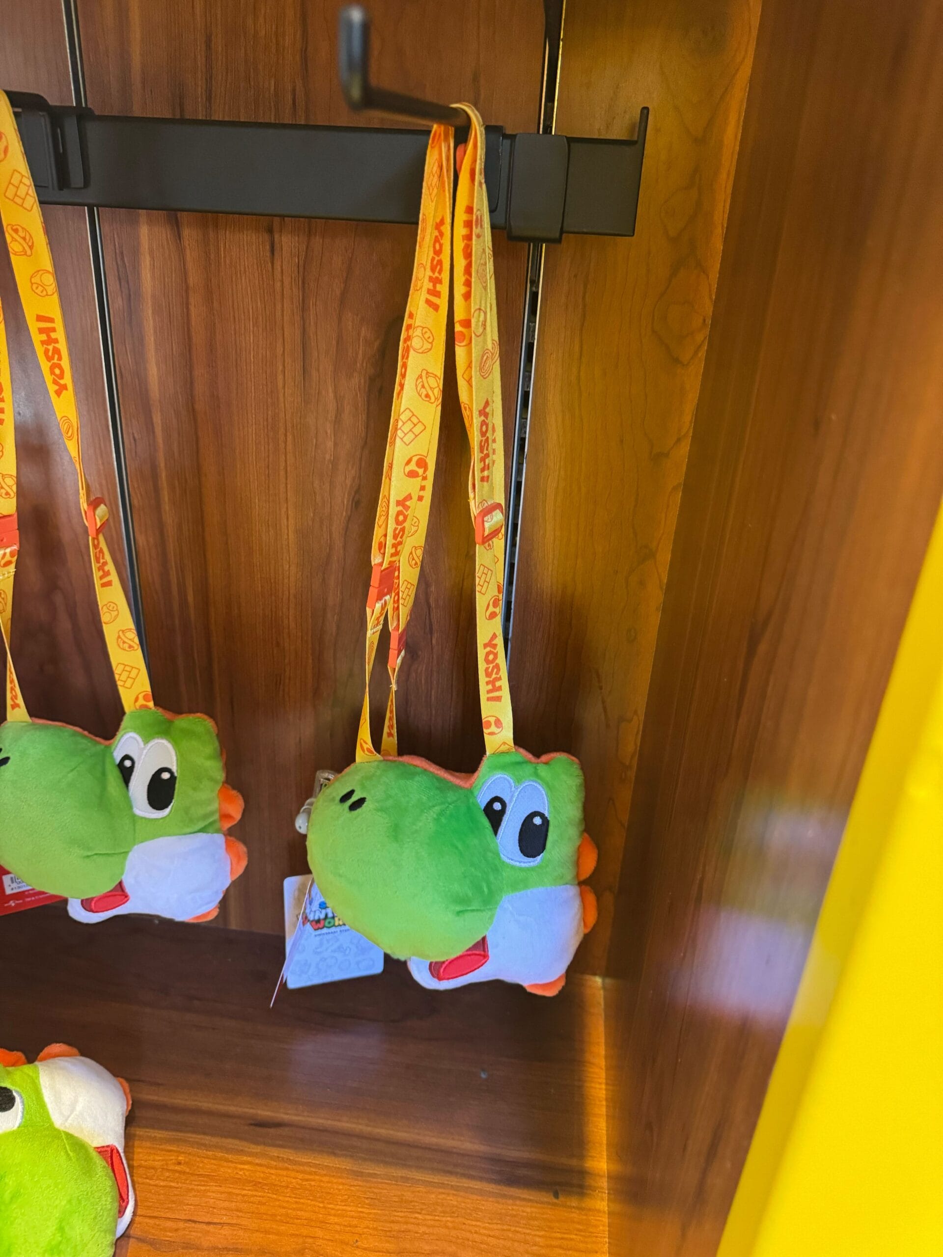 A plush Yoshi purse with a yellow lanyard hangs on a wooden display at Universal Studios Hollywood.