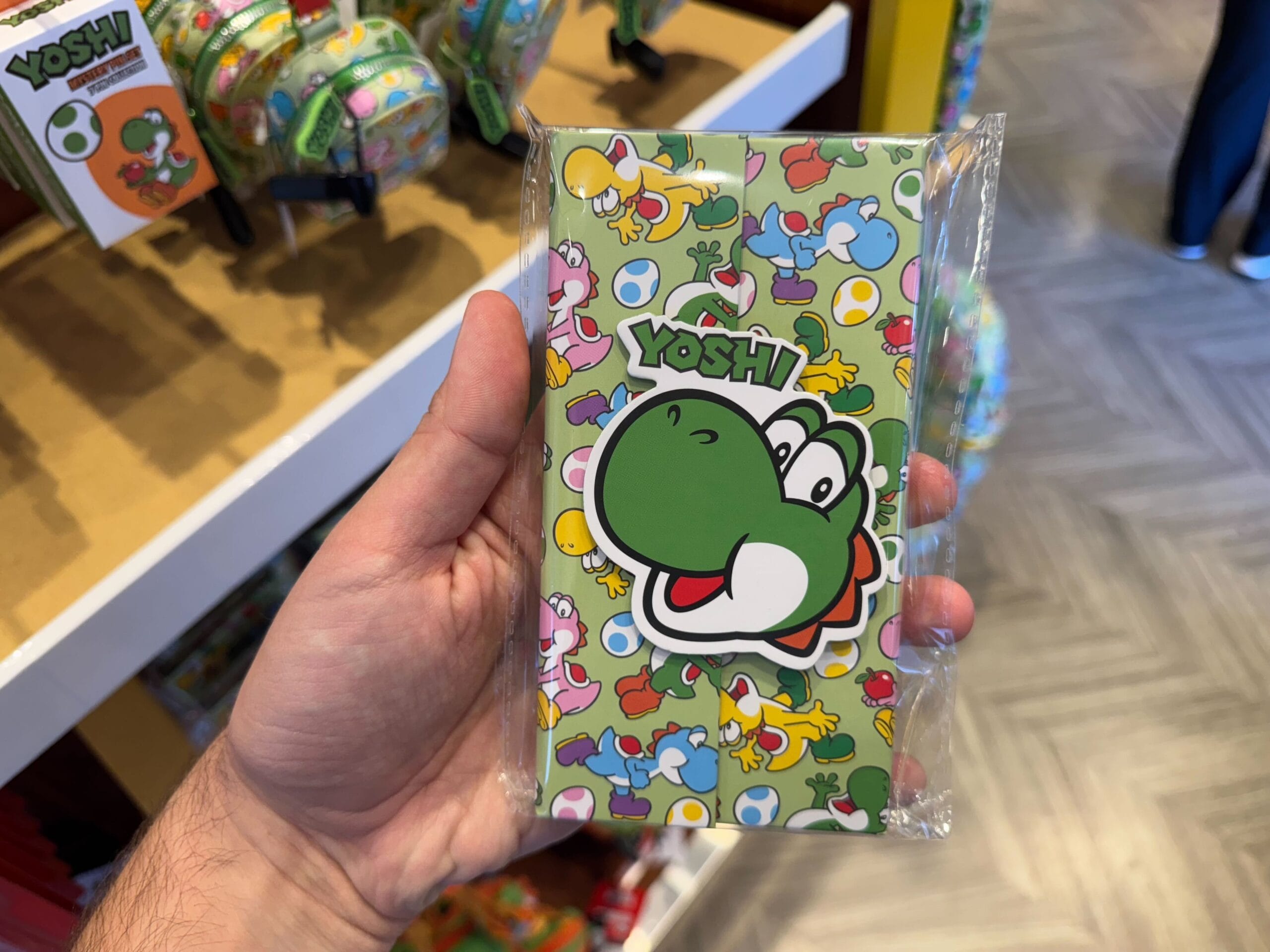 A hand holds a Yoshi-themed notepad, part of colorful Yoshi merchandise at Universal Studios Hollywood.