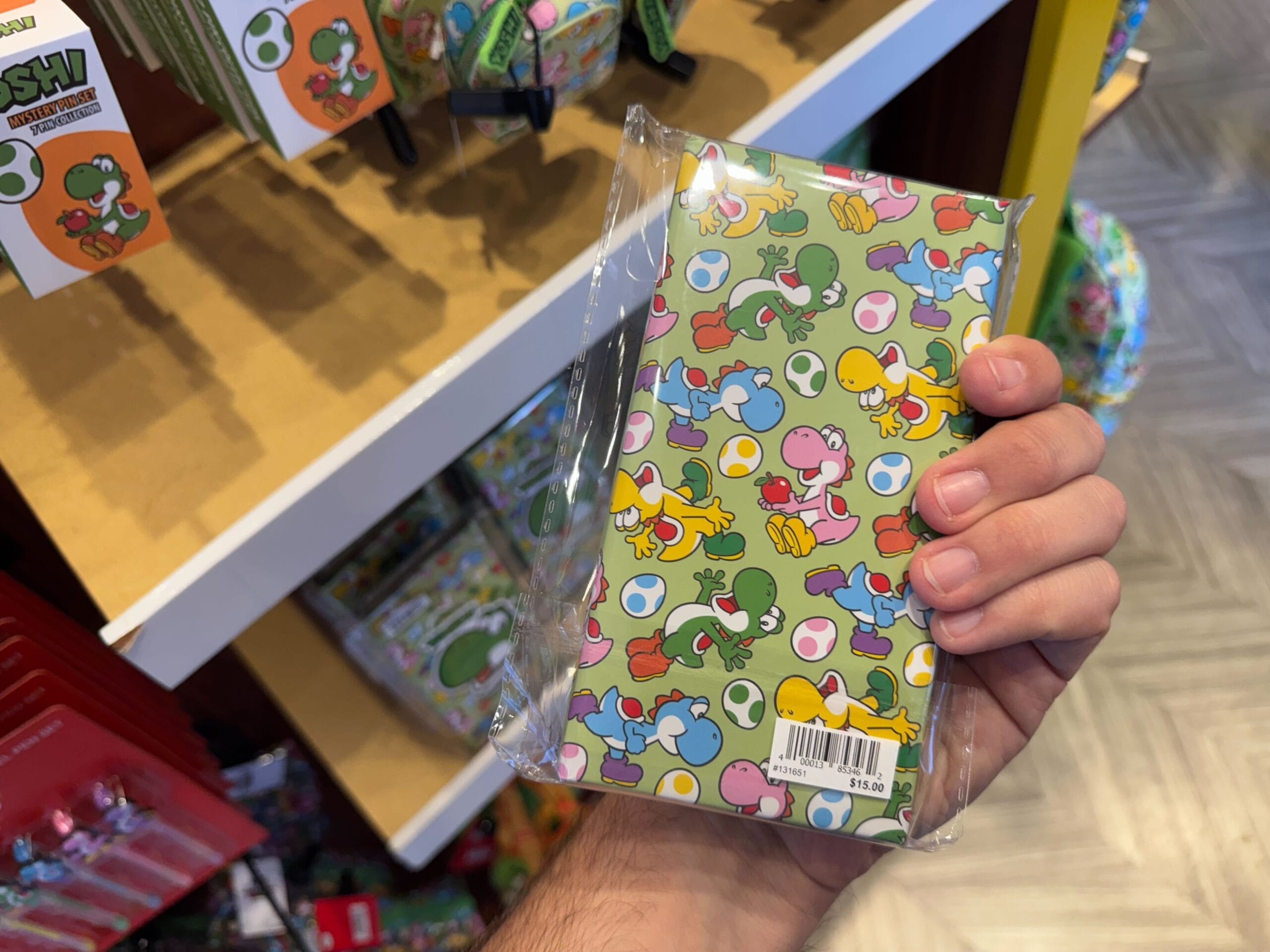 Hand holding a colorful Yoshi-themed notebook, part of exclusive Yoshi merchandise at Universal Studios Hollywood.