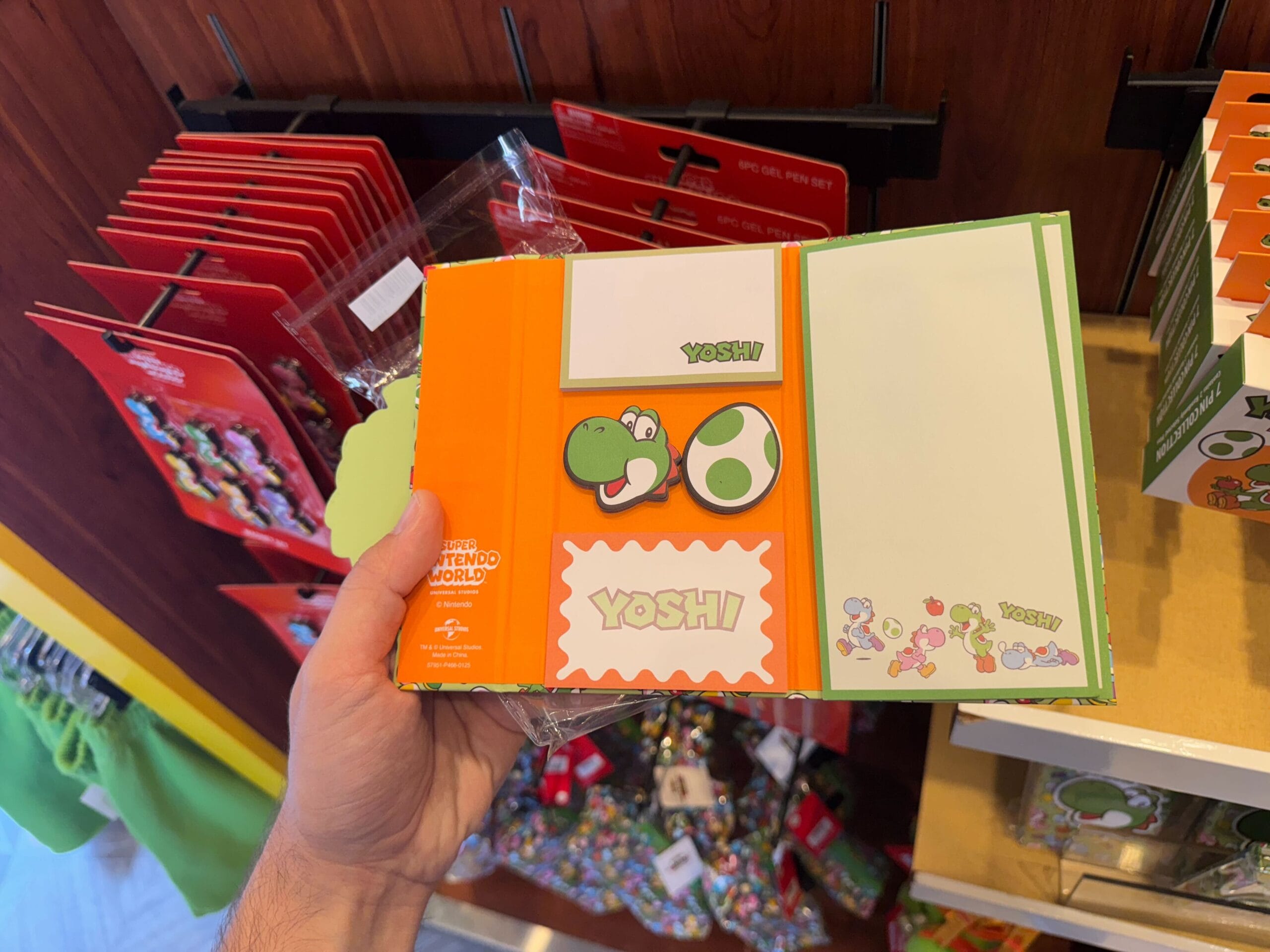 A hand holds Yoshi merchandise—a themed sticky note set—at a Universal Studios Hollywood store display.