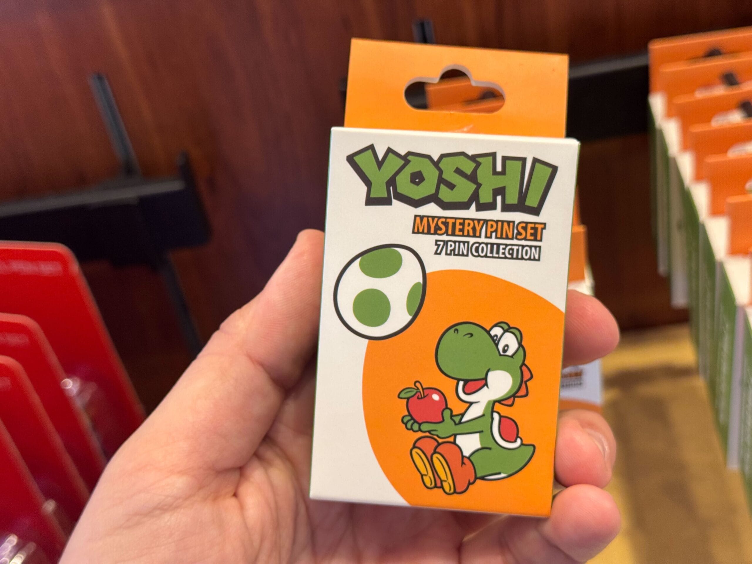 Hand holding a Yoshi merchandise Mystery Pin Set box at Universal Studios Hollywood, featuring Yoshi and an egg illustration.
