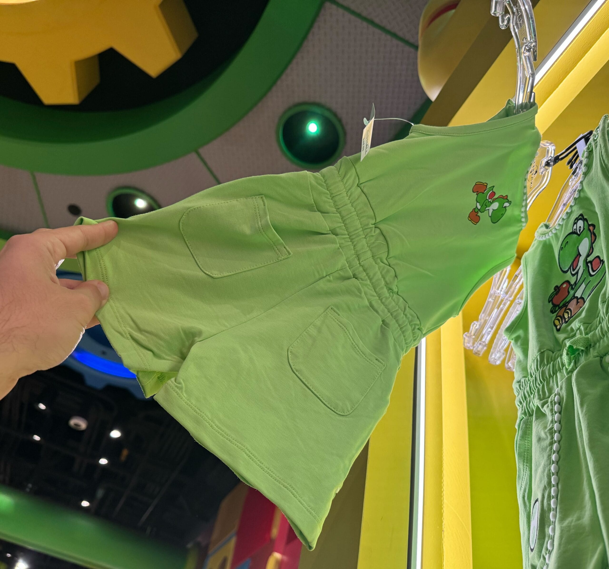 A hand holds up Yoshi merchandise—a green romper—displayed on a rack at Universal Studios Hollywood.