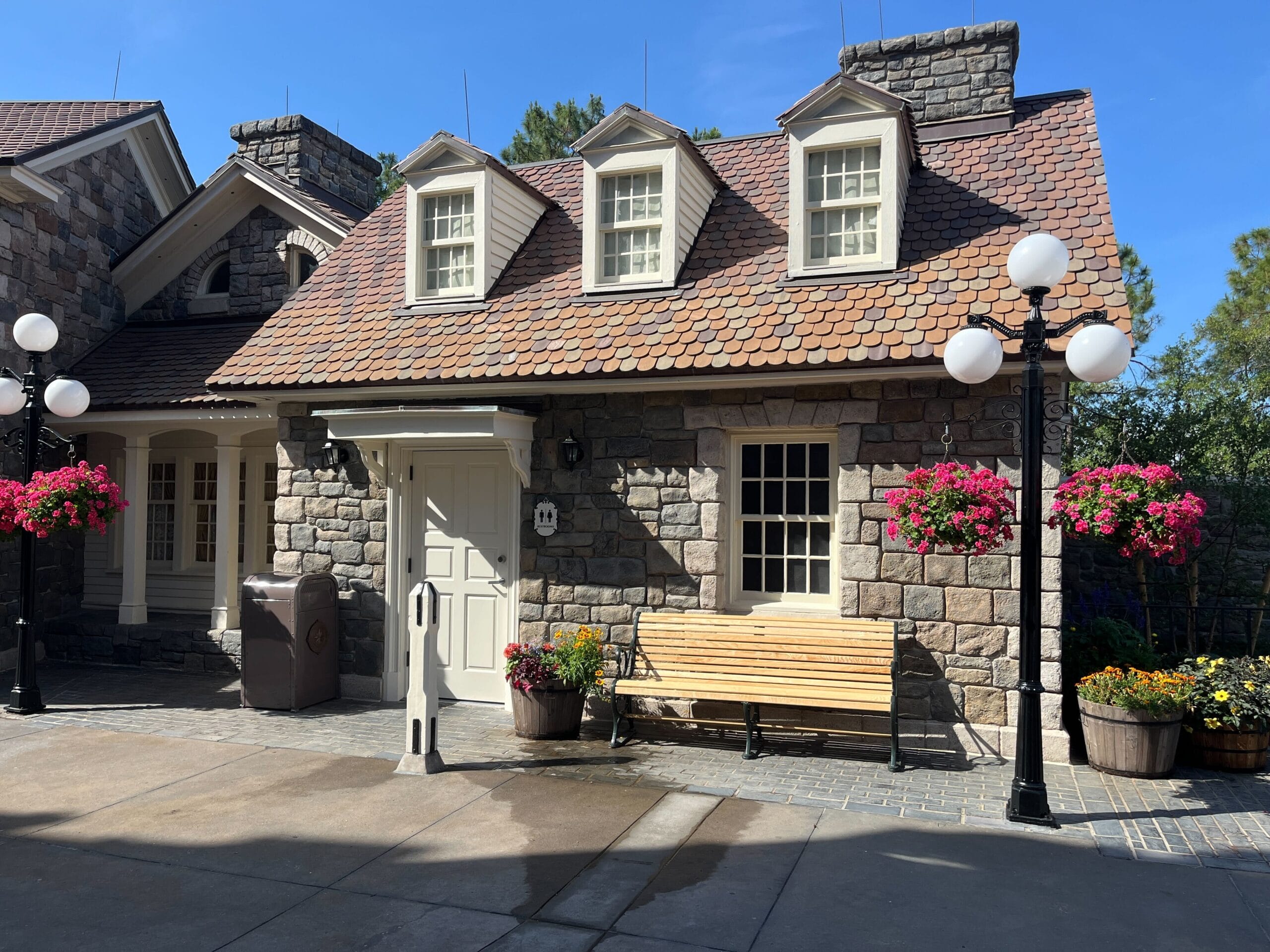 Stone building with dormer windows at EPCOT’s Canada Pavilion, featuring benches, flowers, and public restrooms nearby.