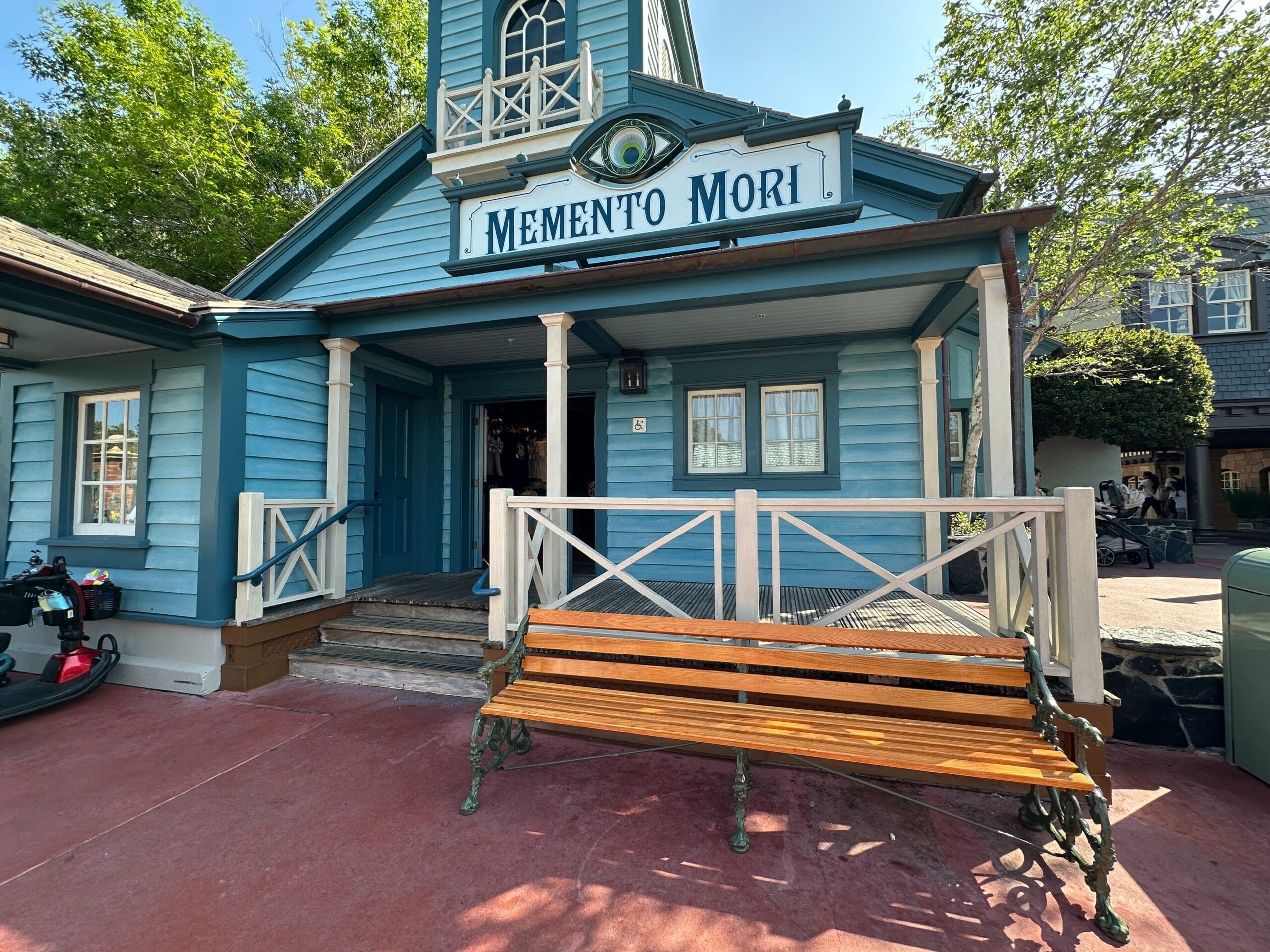 A blue wooden building with a "Memento Mori" sign and a Ghostly Dog Bench, near the Haunted Mansion in Magic Kingdom.