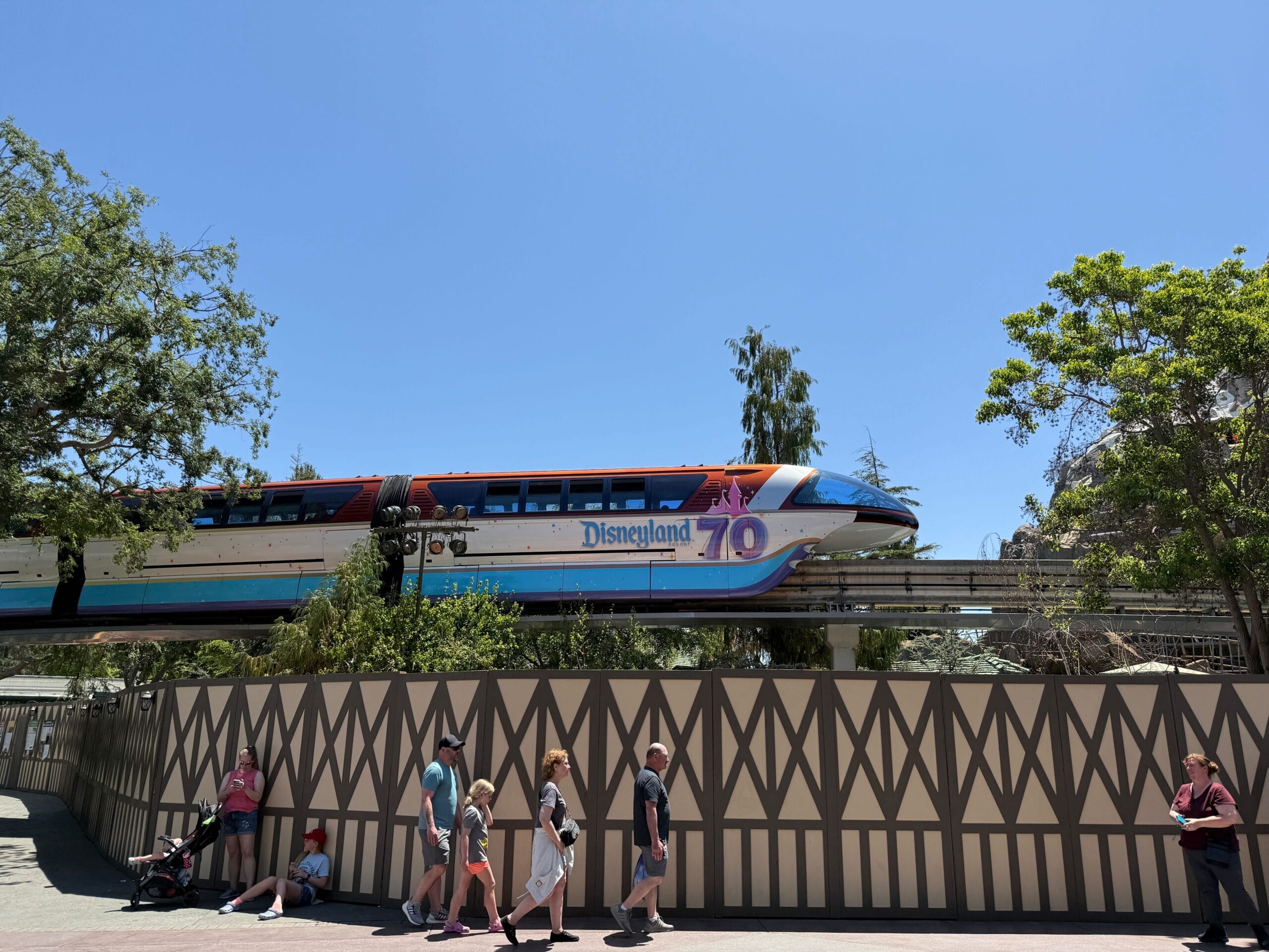 Disneyland Monorail with a new wrap features a "70th Anniversary" logo as it glides above guests on a sunny day.
