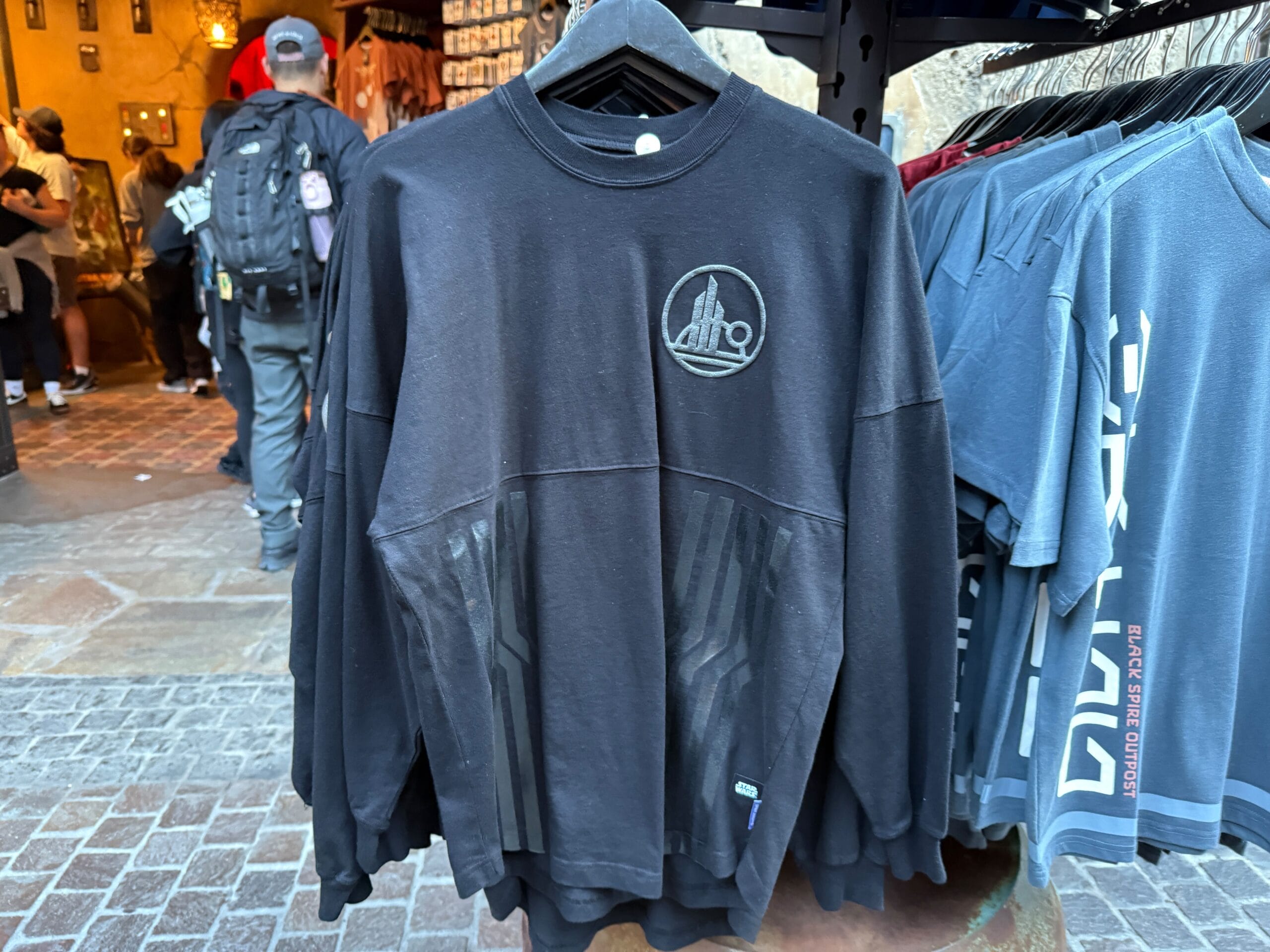 Black Star Wars Spirit Jersey sweatshirt with Death Star logo, hanging on a rack at Disneyland.