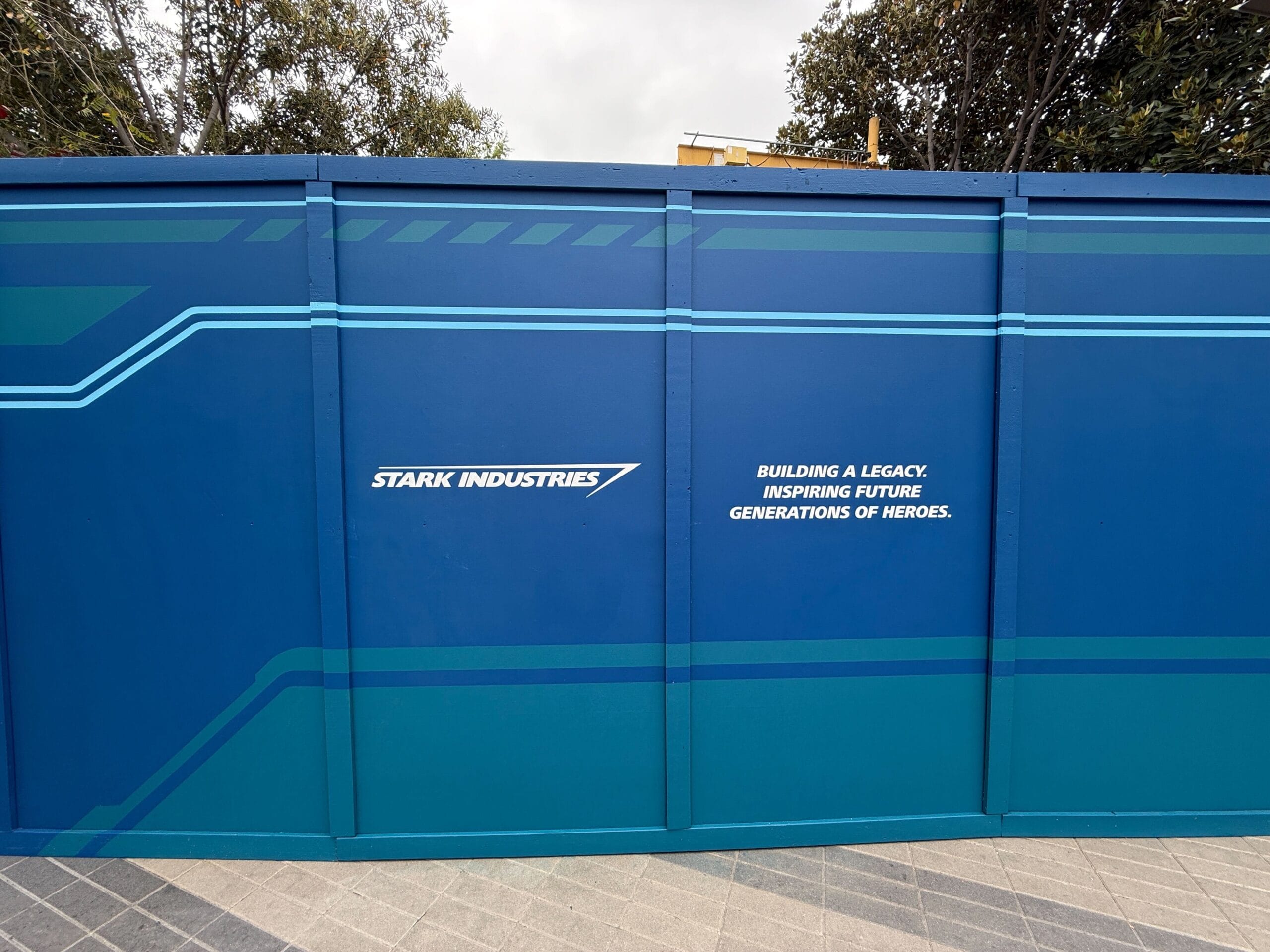 Blue construction walls at Avengers Campus, featuring Stark Industries logo: Building a legacy for future heroes.