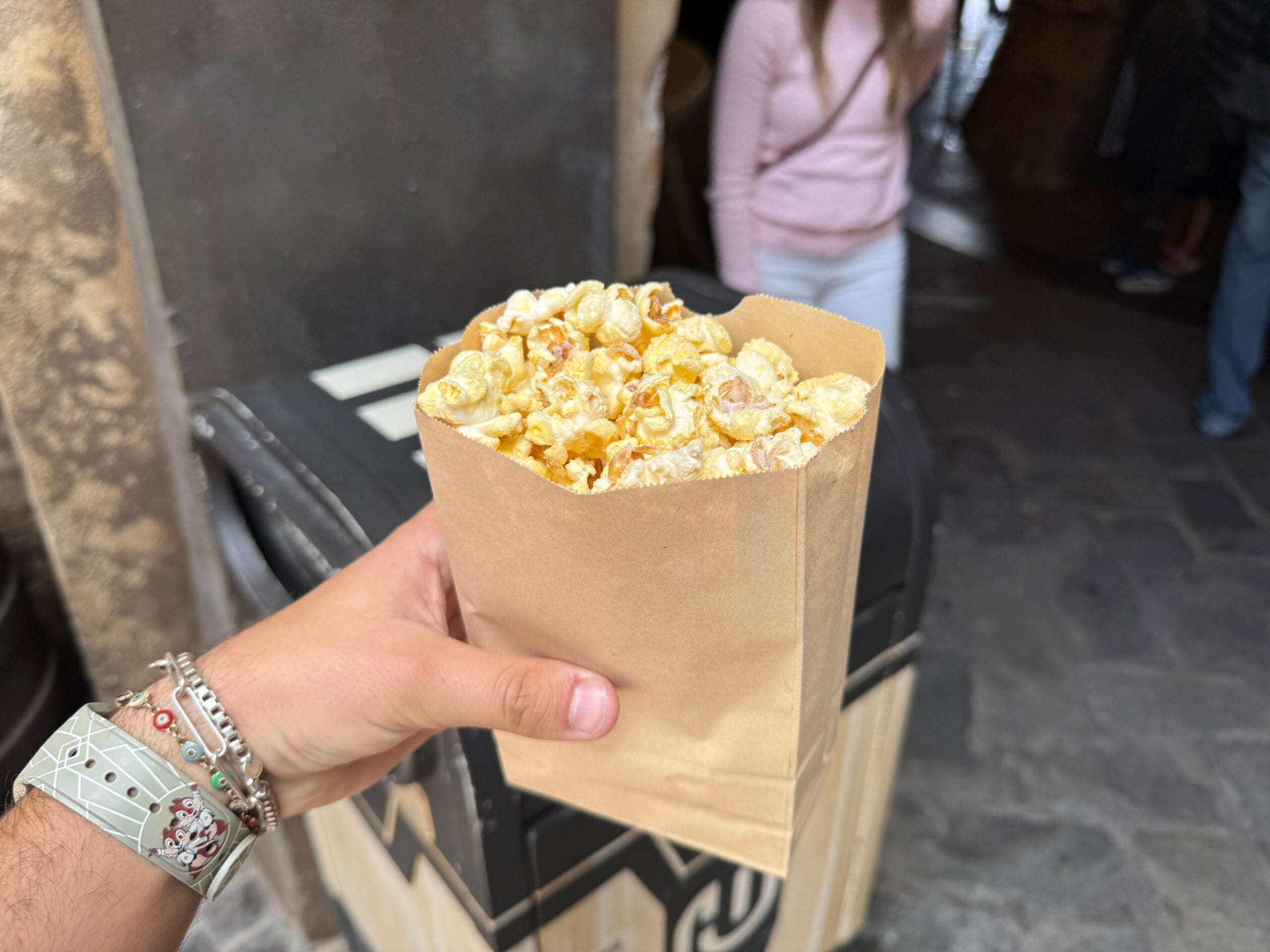 A hand holds a Kat Saka's Kettle popcorn bag near a trash can; people stand in the background at Disneyland Resort.