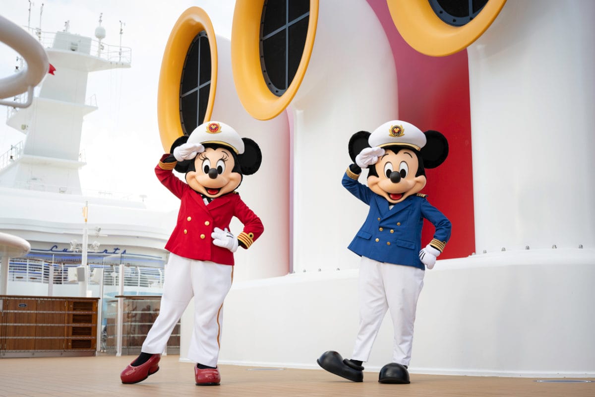 Mickey and Minnie Mouse in captain outfits salute on the deck of a Disney Cruise Line ship.