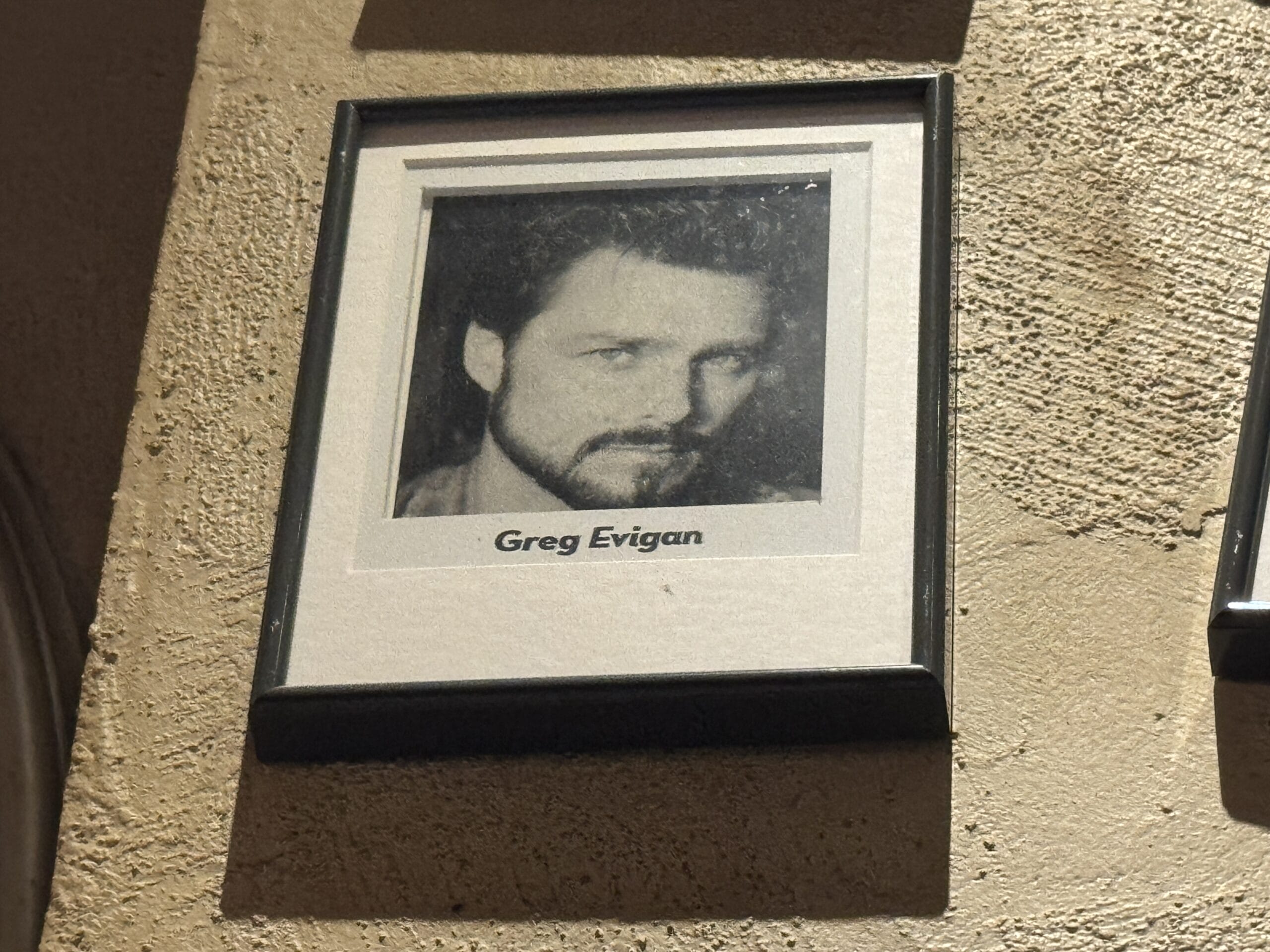 Framed black-and-white portrait labeled "Greg Evigan" among photos at Mama Melrose’s Ristorante Italiano in Disney's Hollywood Studios.