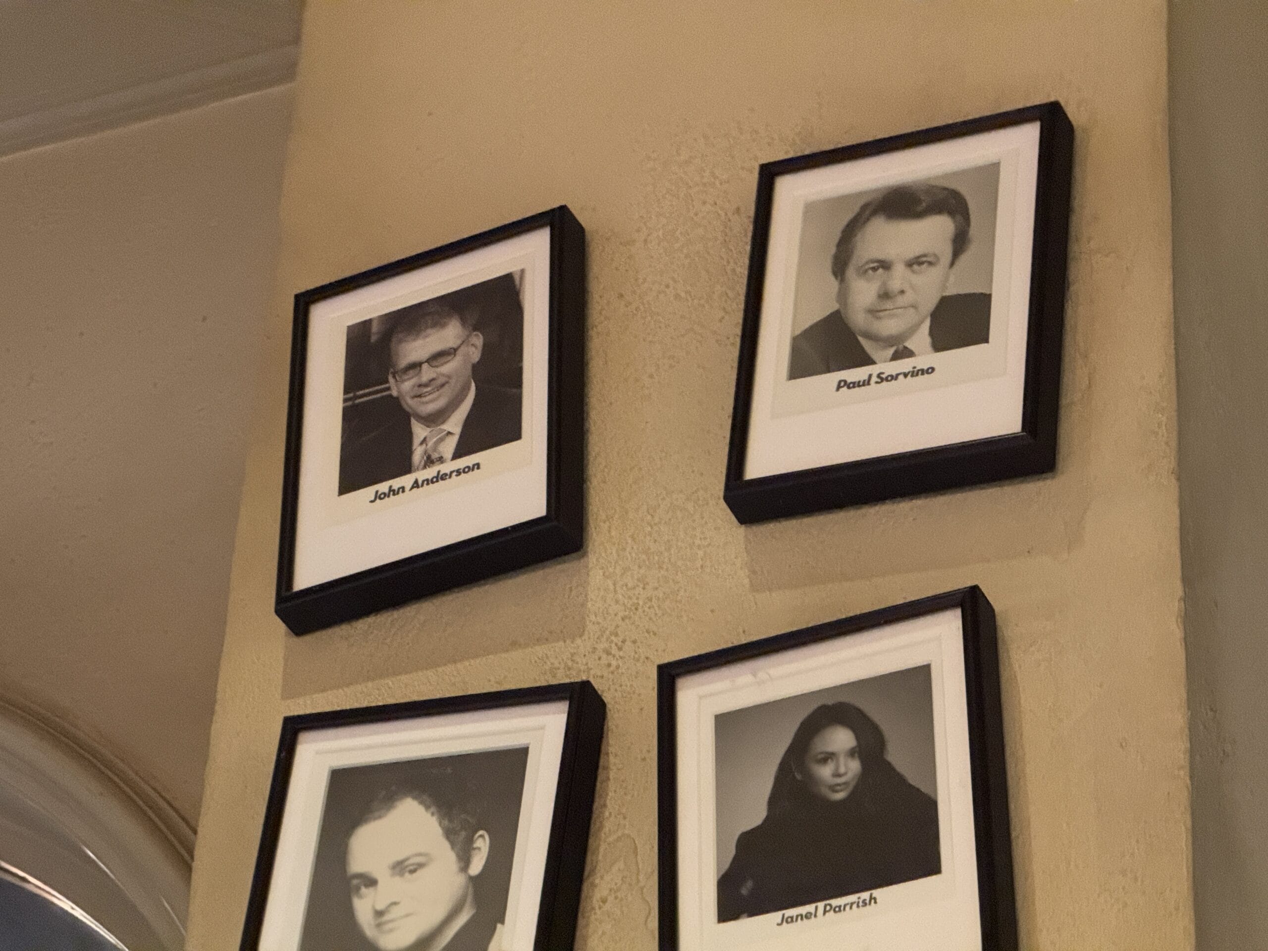 Four framed black-and-white PHOTOS of celebrities hang clustered on a beige wall at Mama Melrose’s Ristorante Italiano.