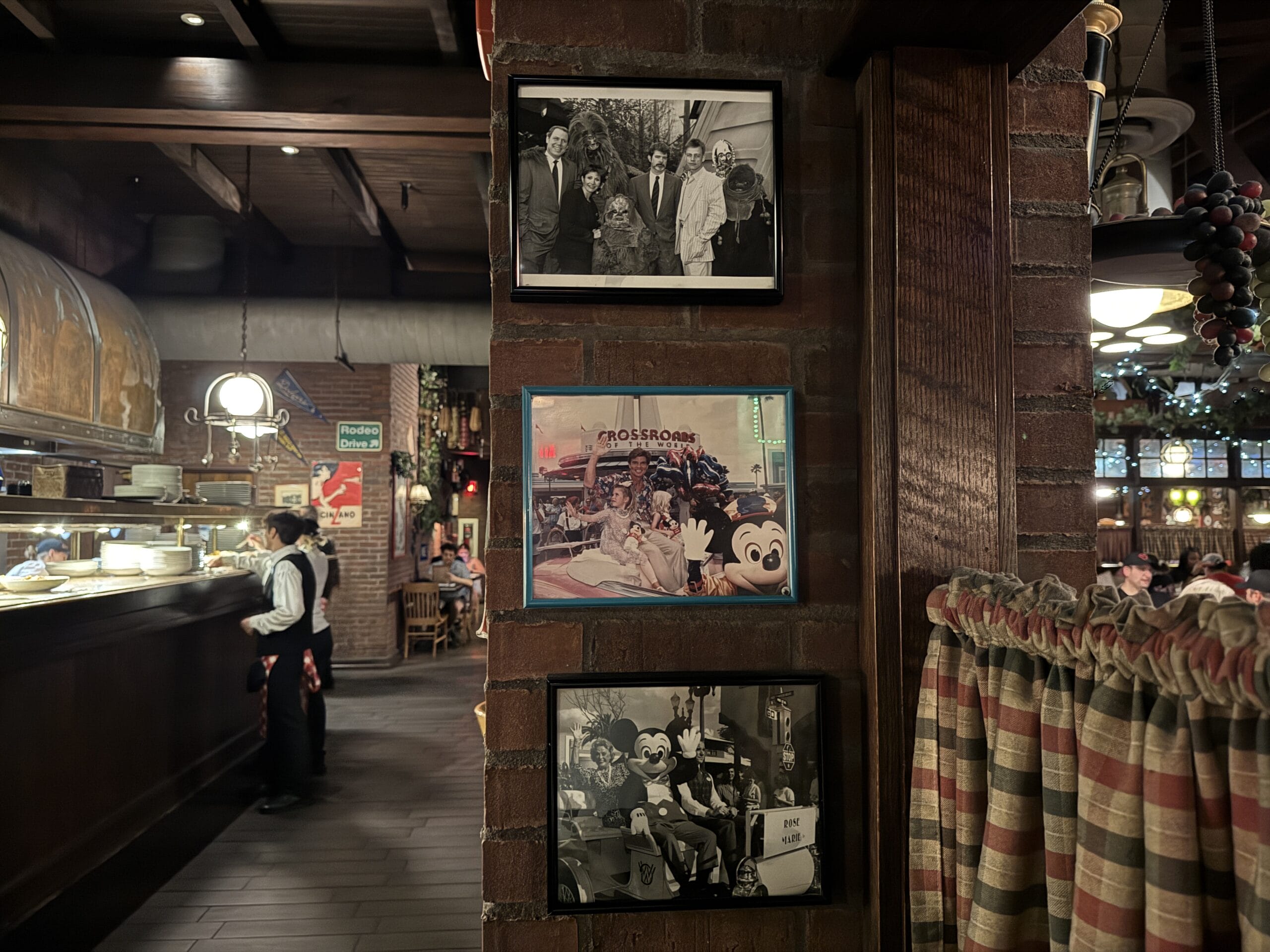 Three photos hang on a brick wall at Mama Melrose’s Ristorante Italiano, with a waiter in the warmly lit background.