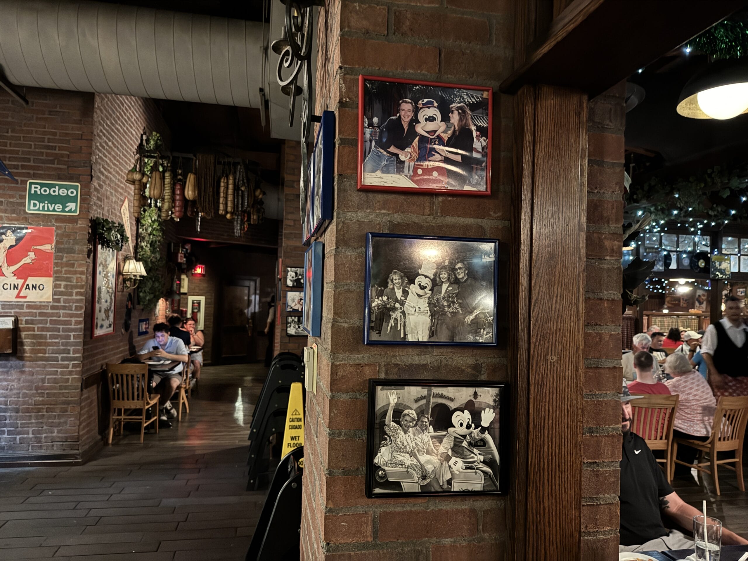 Three framed Mickey Mouse photos hang on a brick wall inside Mama Melrose’s Ristorante Italiano, warmly lit and busy.