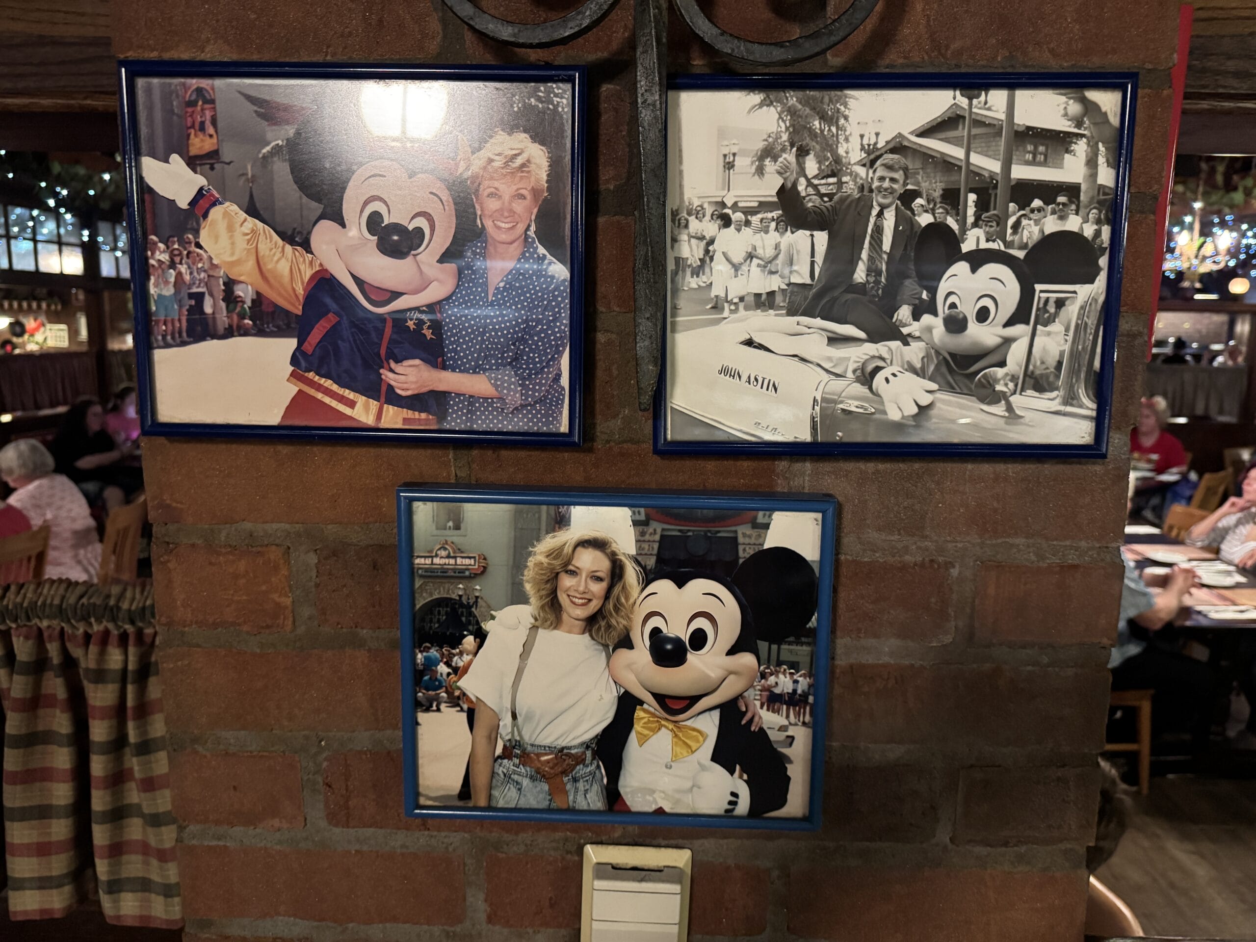 Three framed photos of guests with Mickey Mouse at Mama Melrose’s Ristorante Italiano adorn the brick wall.
