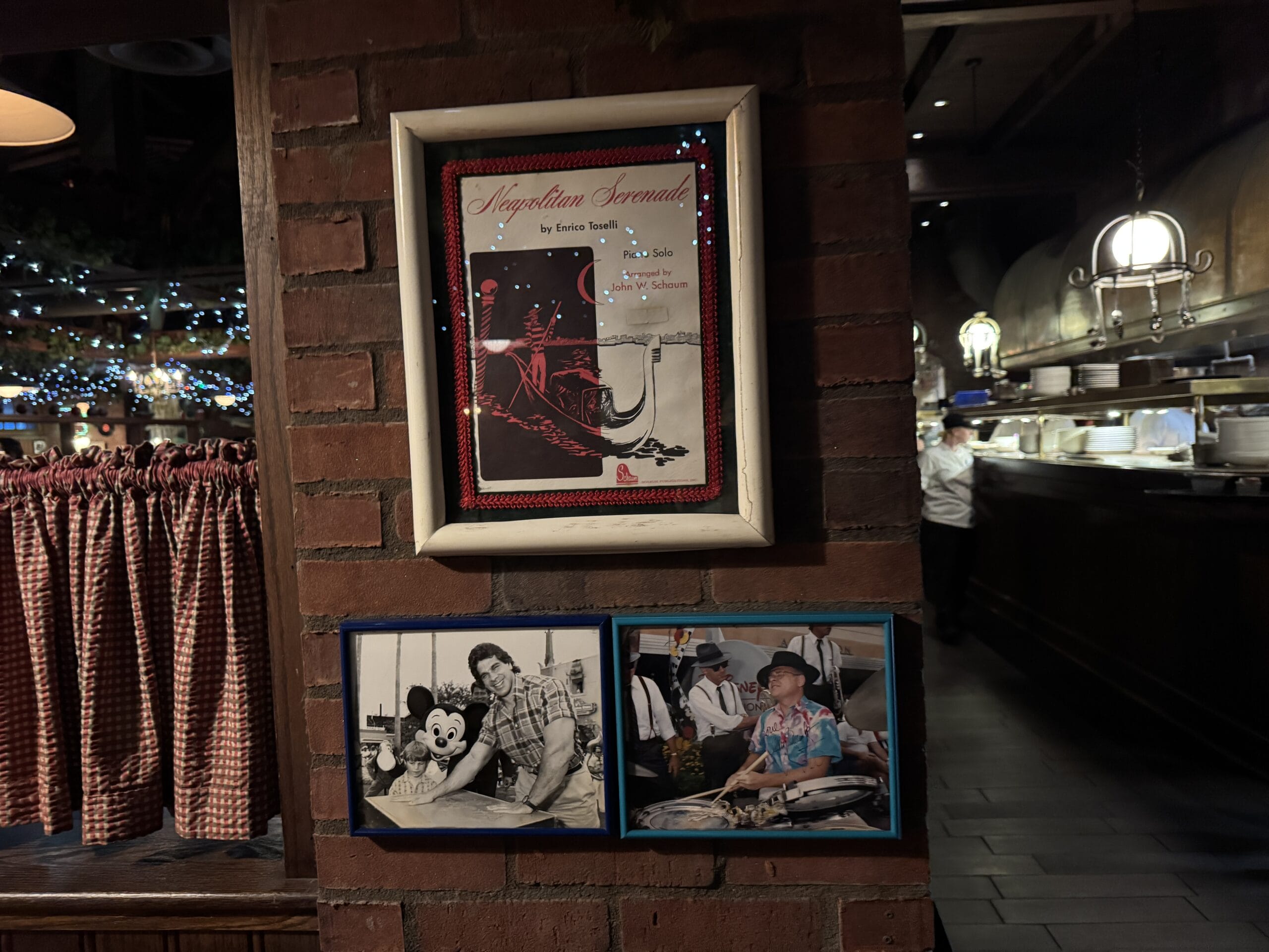Framed photos and a poster hang on a brick wall at Mama Melrose’s Ristorante Italiano in Disney's Hollywood Studios.