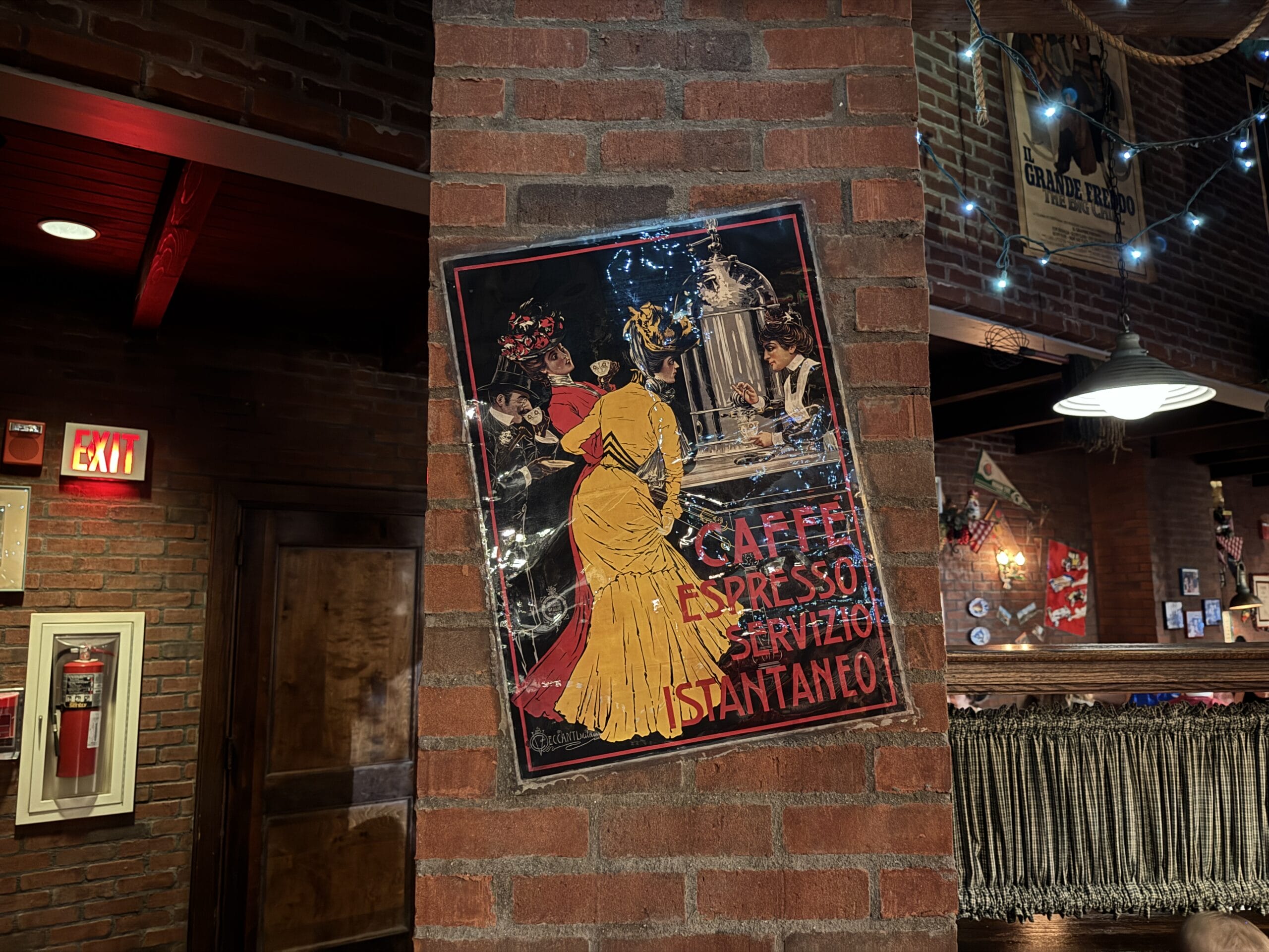 A vintage Italian coffee poster hangs on a brick pillar inside Mama Melrose’s Ristorante Italiano at Disney's Hollywood Studios.