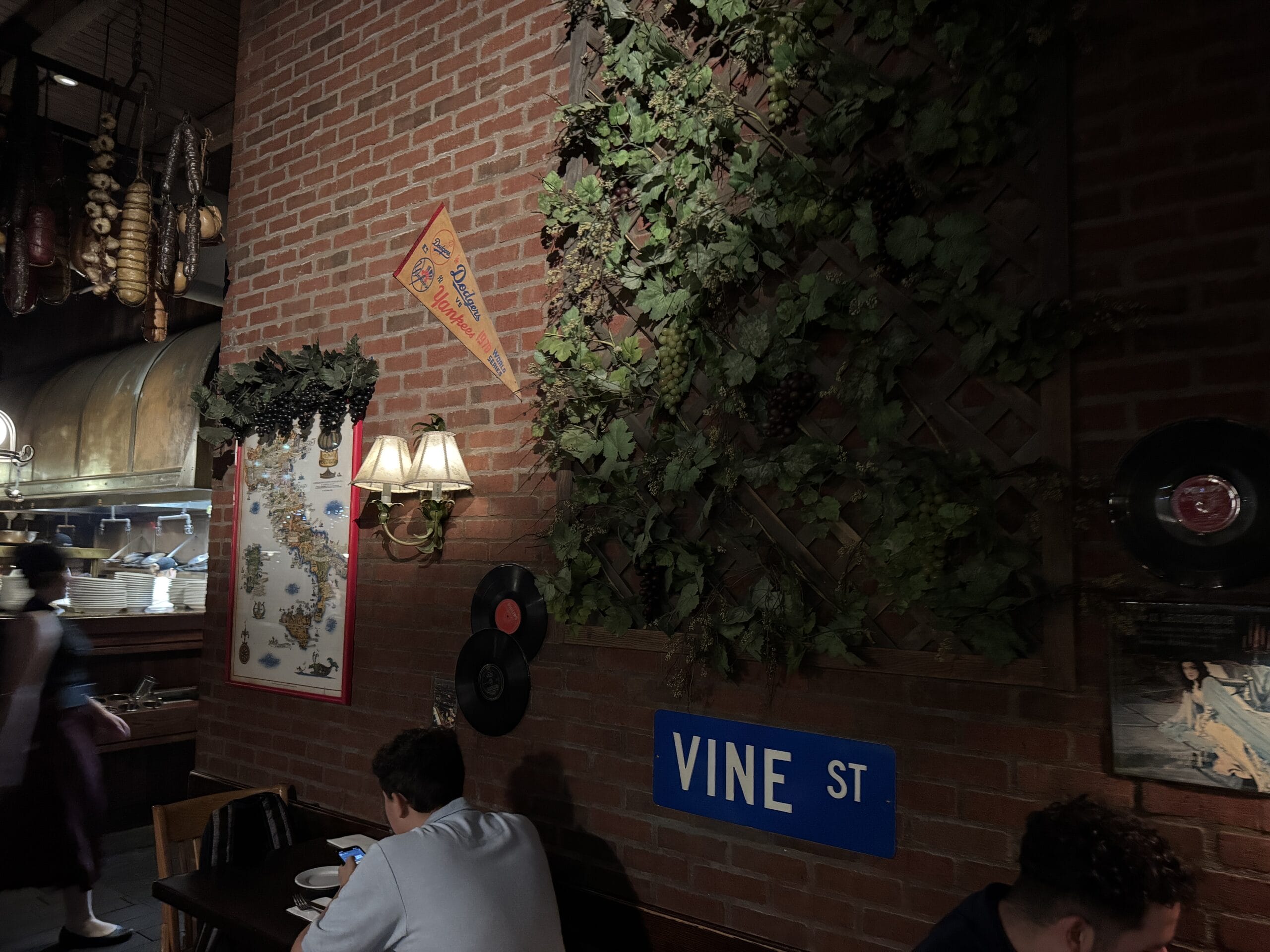 Dimly lit wall at Mama Melrose’s Ristorante Italiano in Disney's Hollywood Studios, with "Vine St" sign, plants, and records.