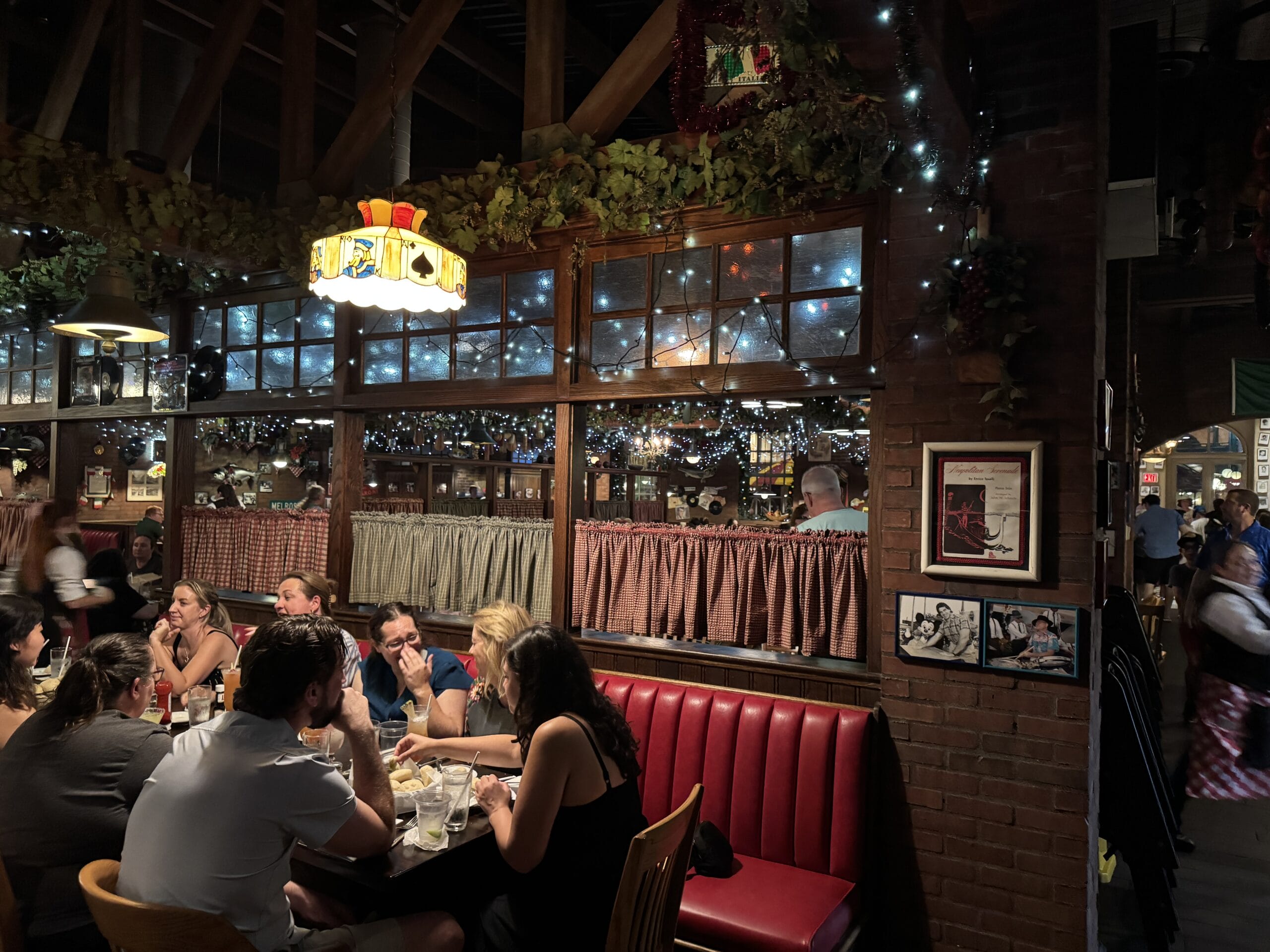 A group dines at Mama Melrose’s Ristorante Italiano in Disney's Hollywood Studios, surrounded by twinkling lights and cozy decor.