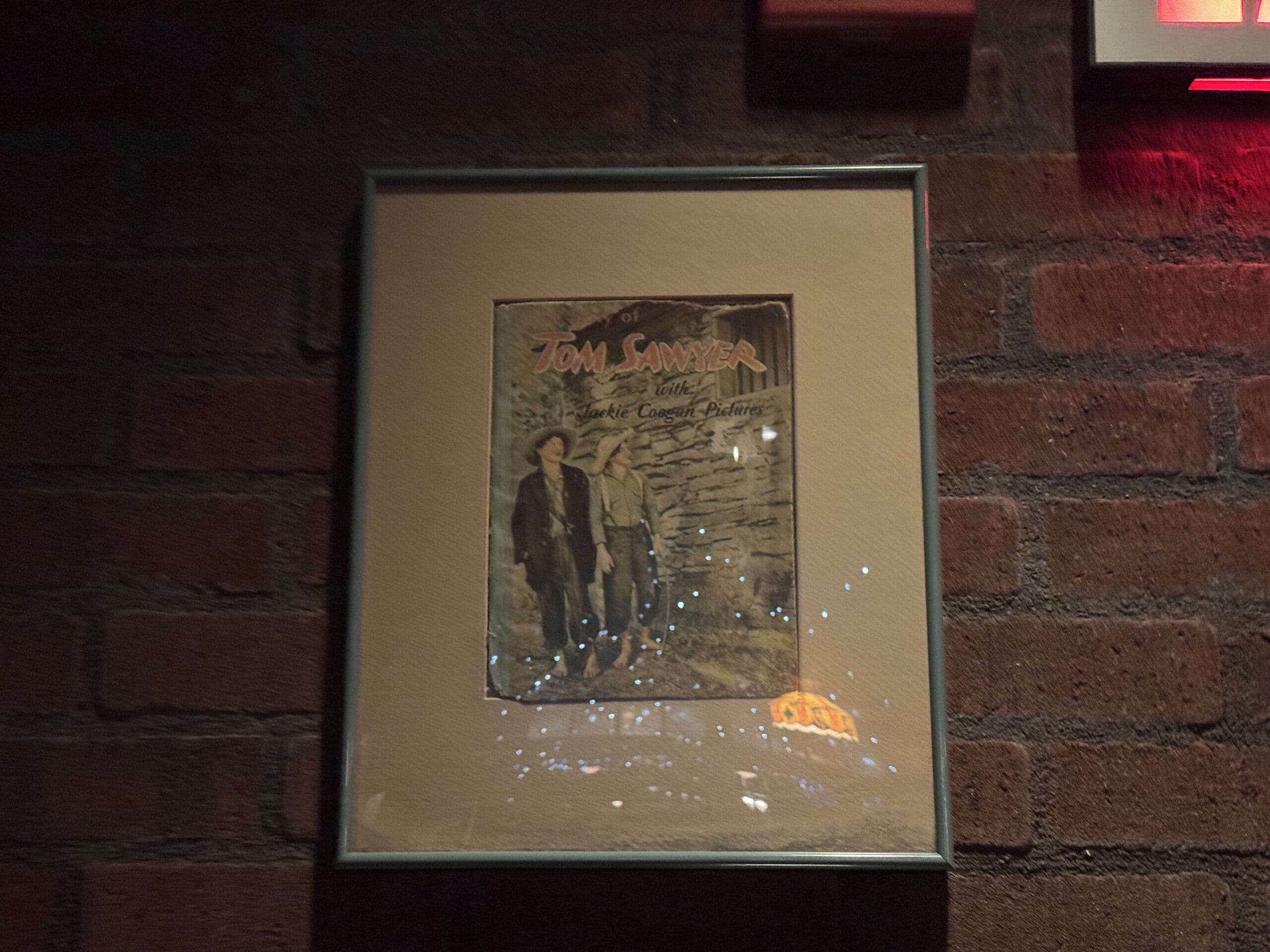 Framed poster of "Tom Sawyer" featuring two boys, with reflections, seen at Mama Melrose’s Ristorante Italiano.