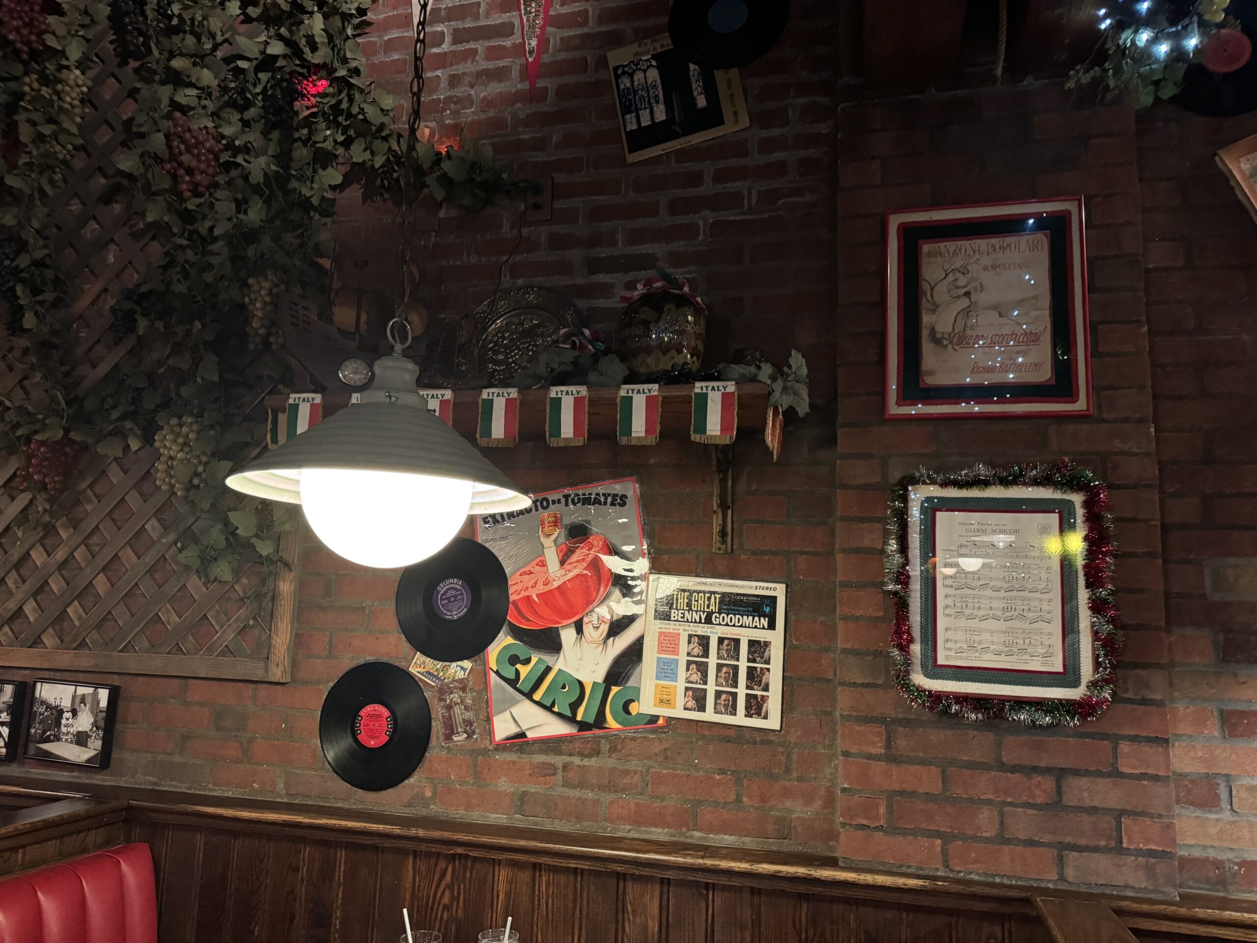 Dimly lit brick wall at Mama Melrose’s Ristorante Italiano featuring records, photos, Italian flags, and vintage memorabilia.