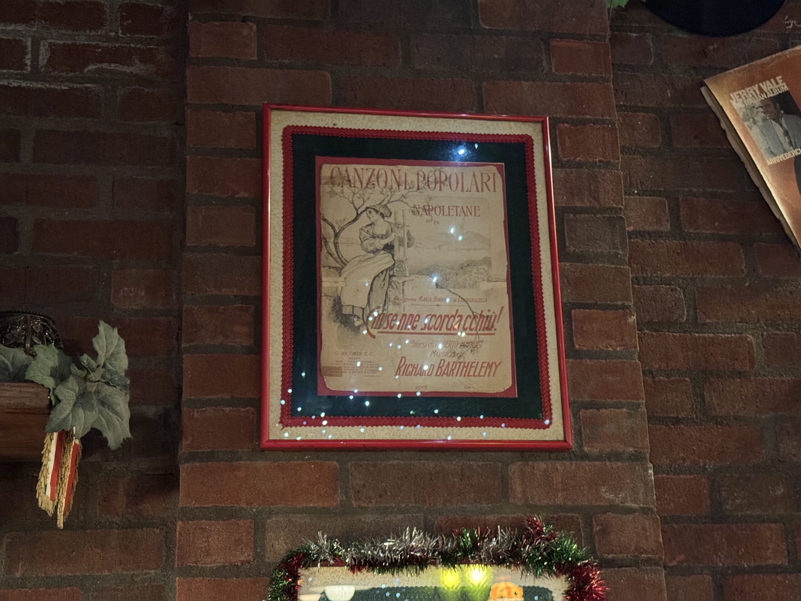 Framed vintage Italian poster at Mama Melrose’s Ristorante Italiano, with garland and lights—perfect for festive photos.