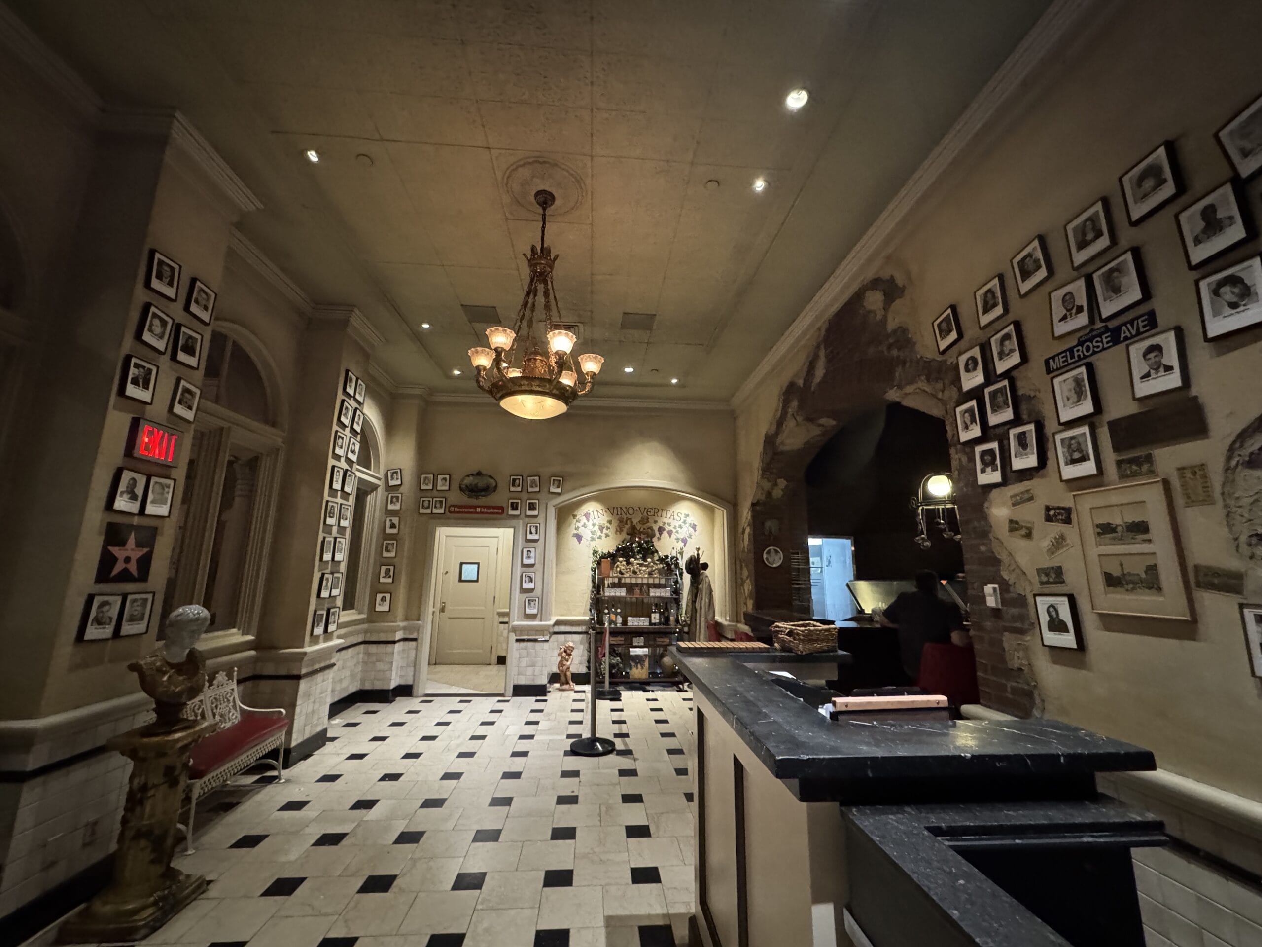 Dimly lit vintage-style lobby at Mama Melrose’s Ristorante Italiano with photos on the walls and a chandelier overhead.