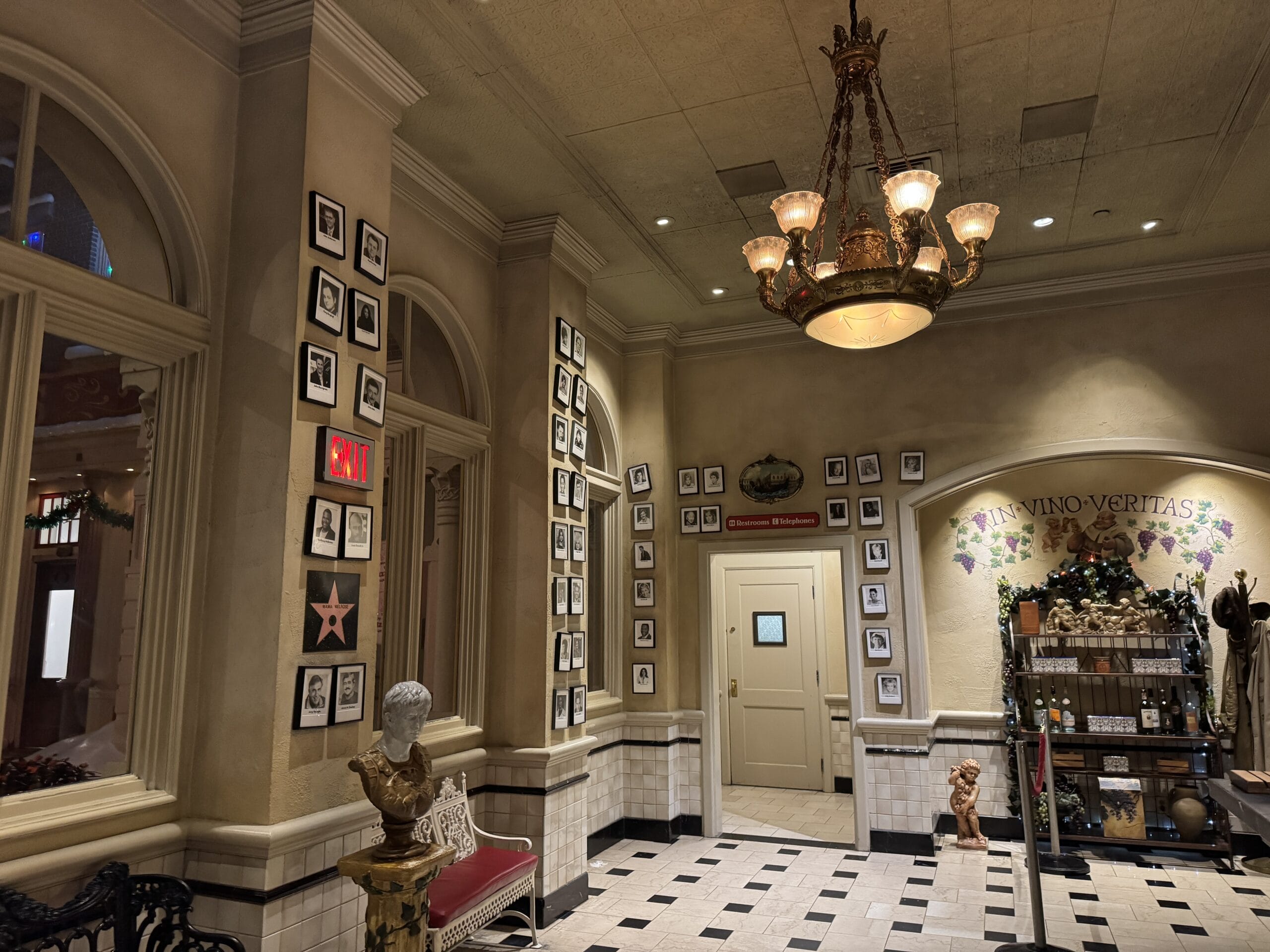 Elegant hallway with photos, statues, chandelier, and a shelf near a door labeled "Vino Veritas" at Disney's Hollywood Studios.