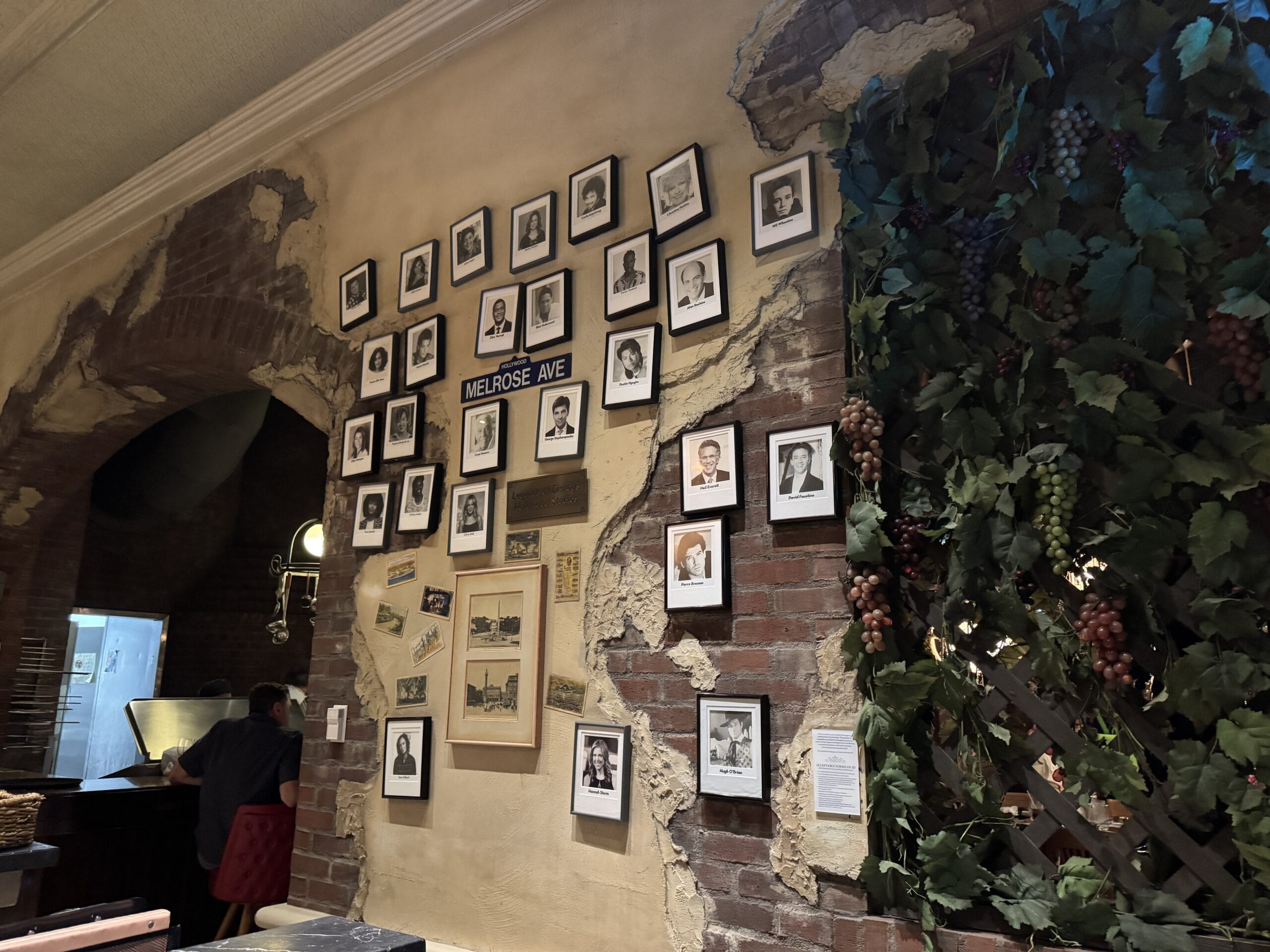 Wall with framed photos, "Melrose Ave" sign, and grapevine decor evoke Mama Melrose’s Ristorante Italiano at Disney's Hollywood Studios.