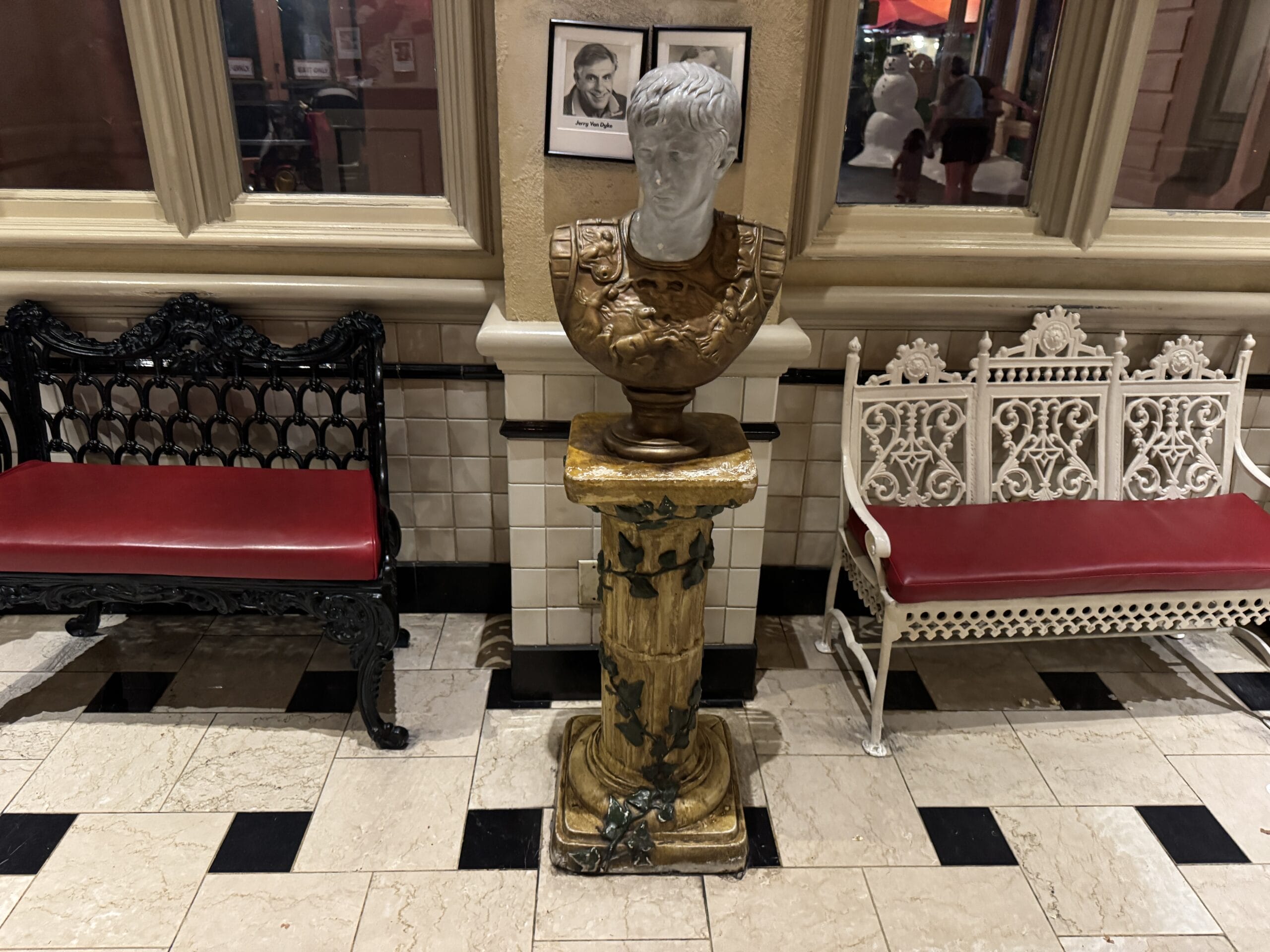 Bust of a man on a marble pedestal at Mama Melrose’s Ristorante Italiano, with framed photos on the wall behind.