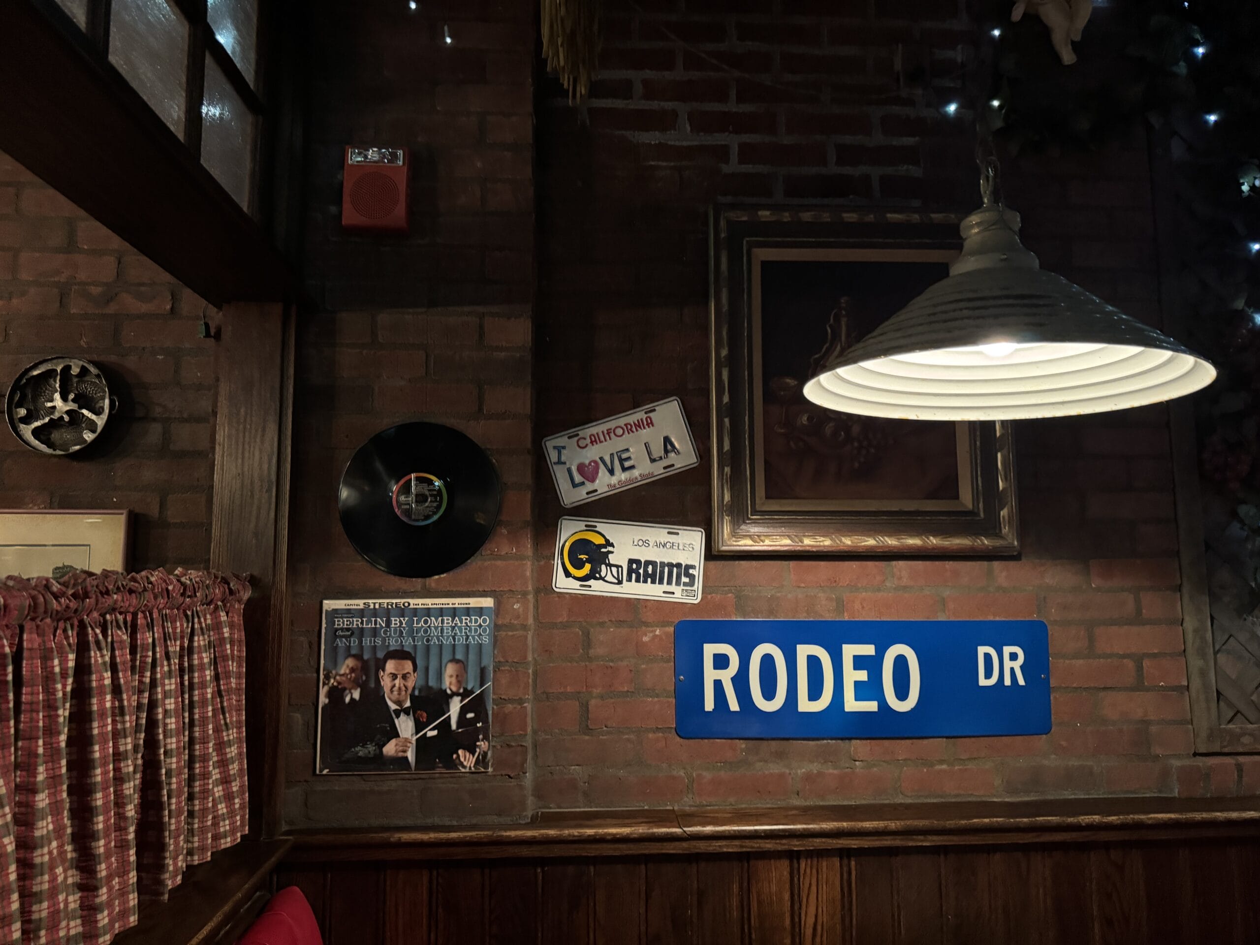 Brick wall at Mama Melrose’s Ristorante Italiano with vintage photos, LA signs, Rams logo, and a blue Rodeo Dr sign.