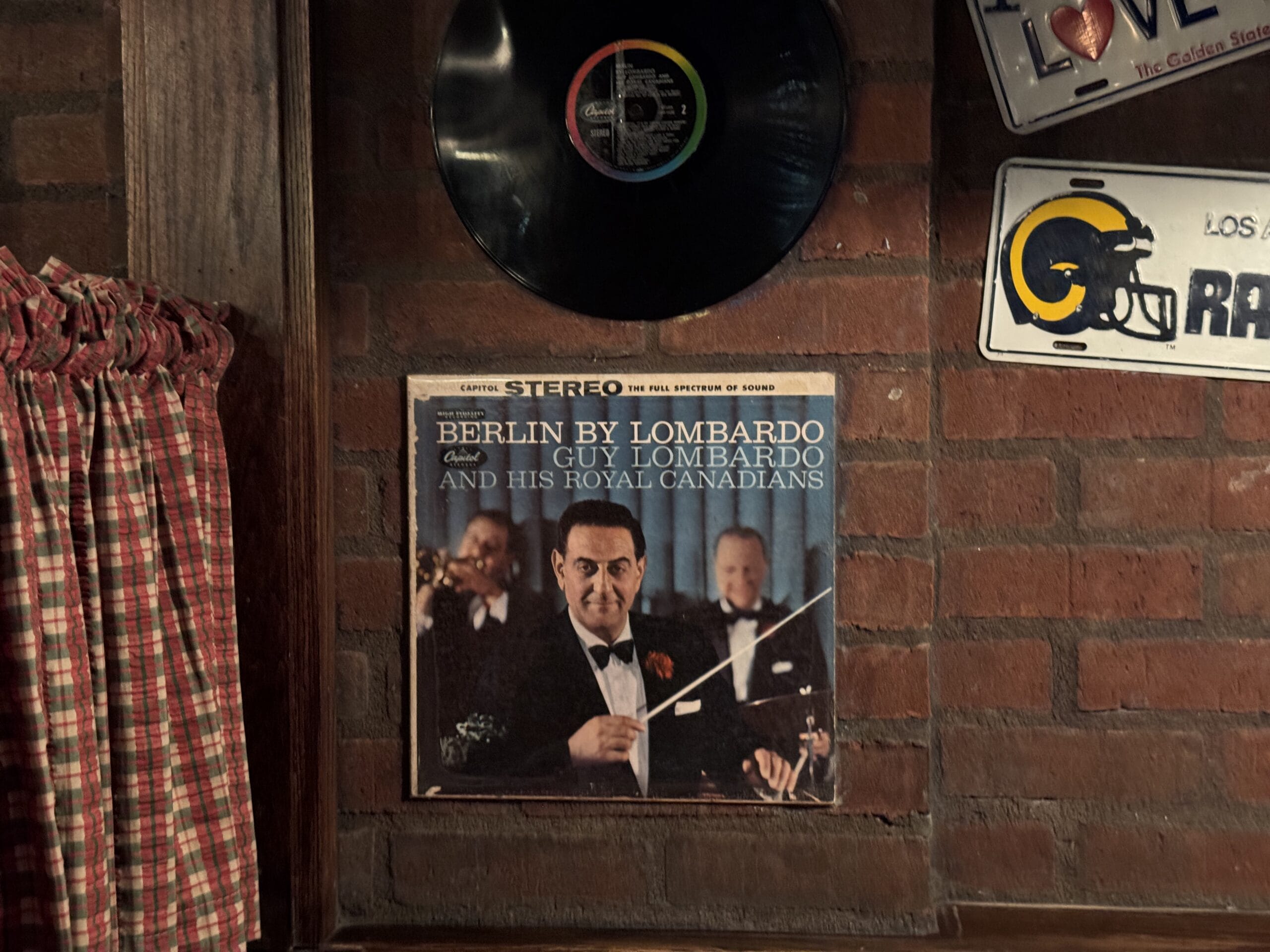 Album cover of "Berlin by Lombardo" at Mama Melrose’s Ristorante Italiano, displayed under a vinyl record on a brick wall.