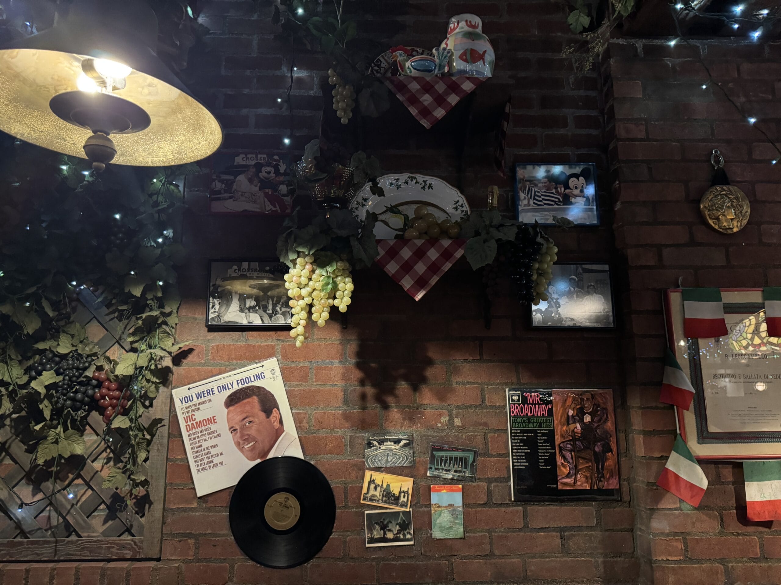 Brick wall at Mama Melrose’s Ristorante Italiano adorned with vintage photos, records, and grapes under warm, dim lighting.