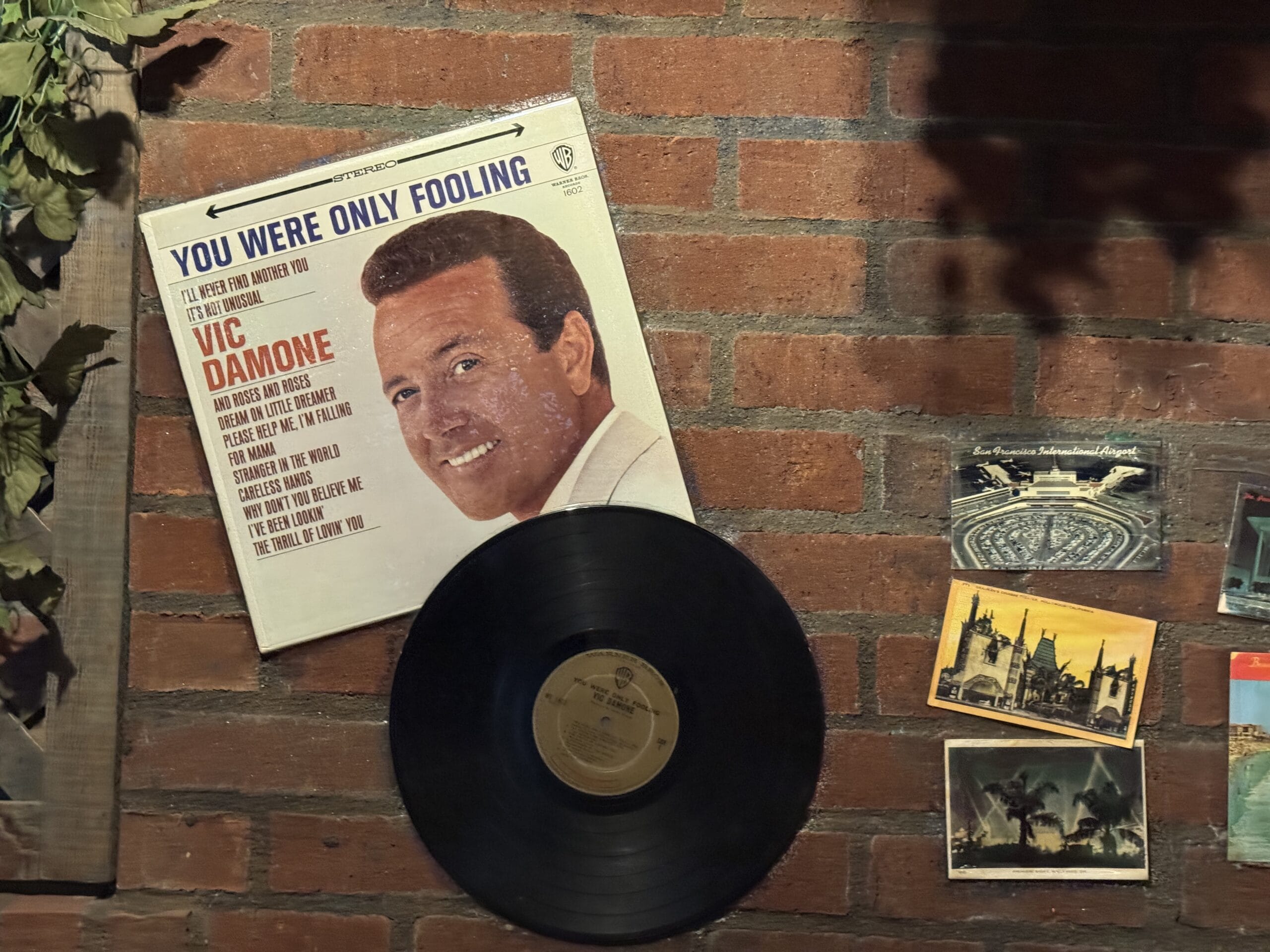 A Vic Damone vinyl and album cover hang on a brick wall at Mama Melrose’s Ristorante Italiano with vintage photos.
