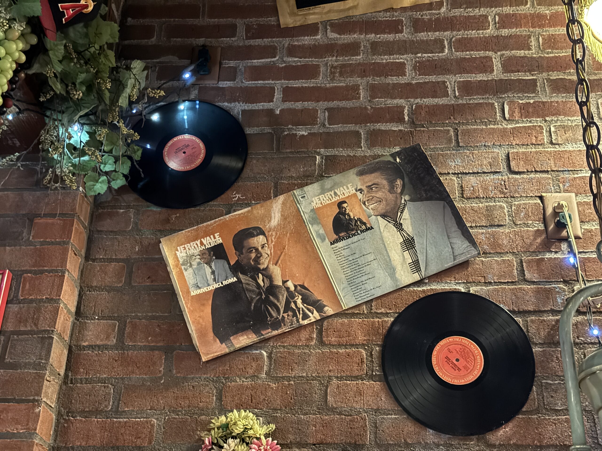 Two vinyl records and an open Jerry Vale album are displayed on a brick wall at Mama Melrose’s Ristorante Italiano.