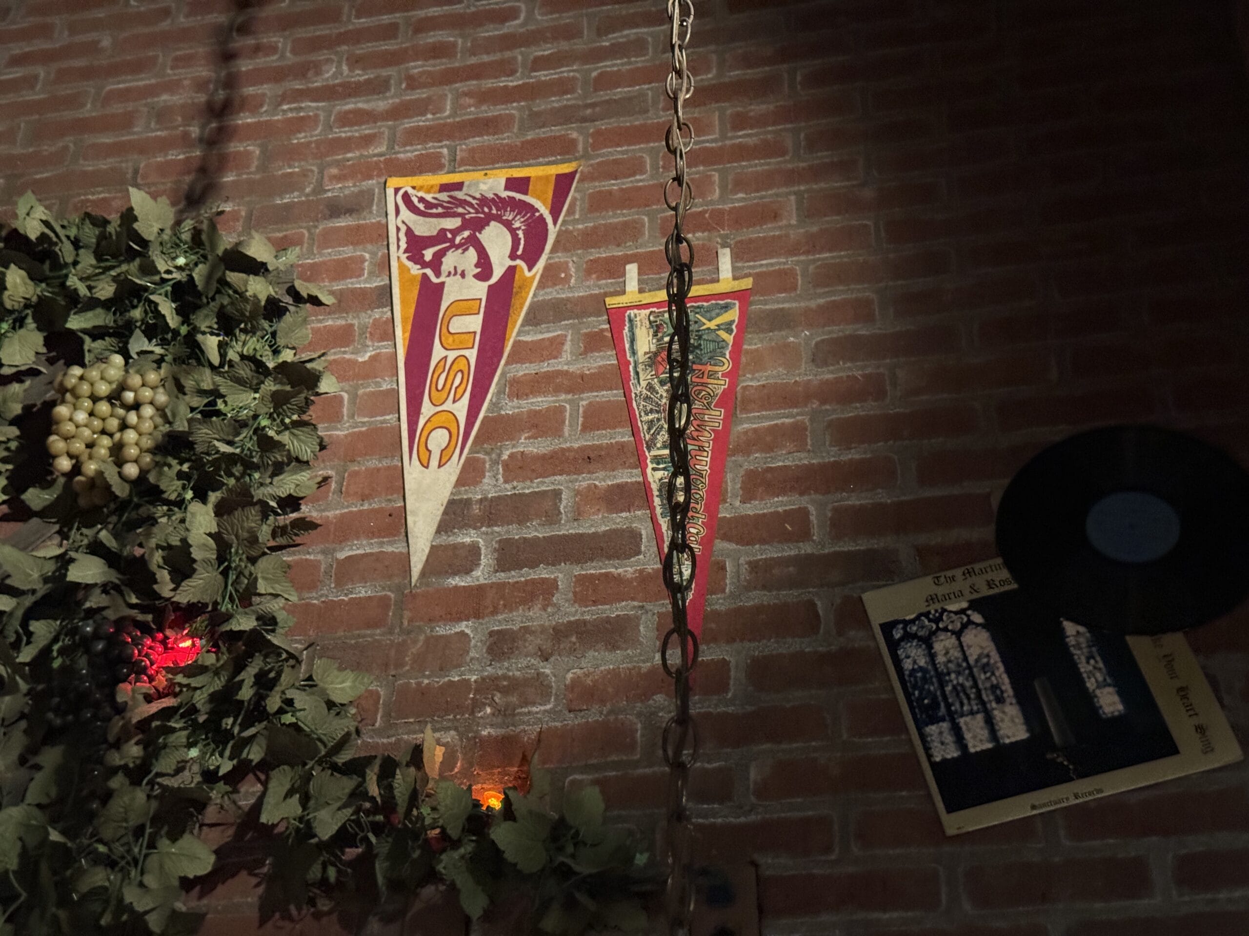 Two vintage college pennants, a vinyl record, and photos decorate the brick wall at Mama Melrose’s Ristorante Italiano.