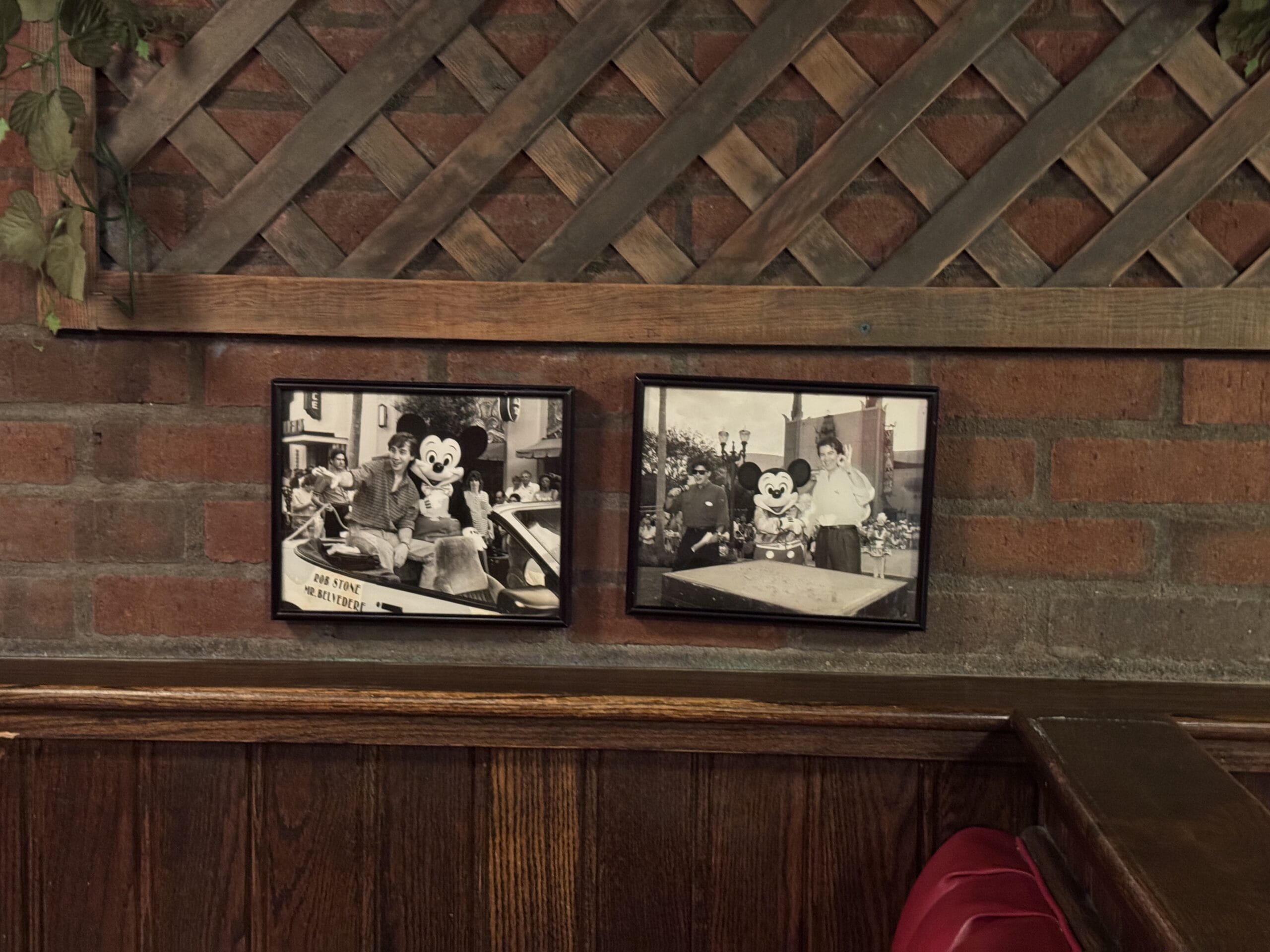 Two framed PHOTOS of people with a Mickey Mouse mascot hang above wood paneling at Mama Melrose’s Ristorante Italiano.
