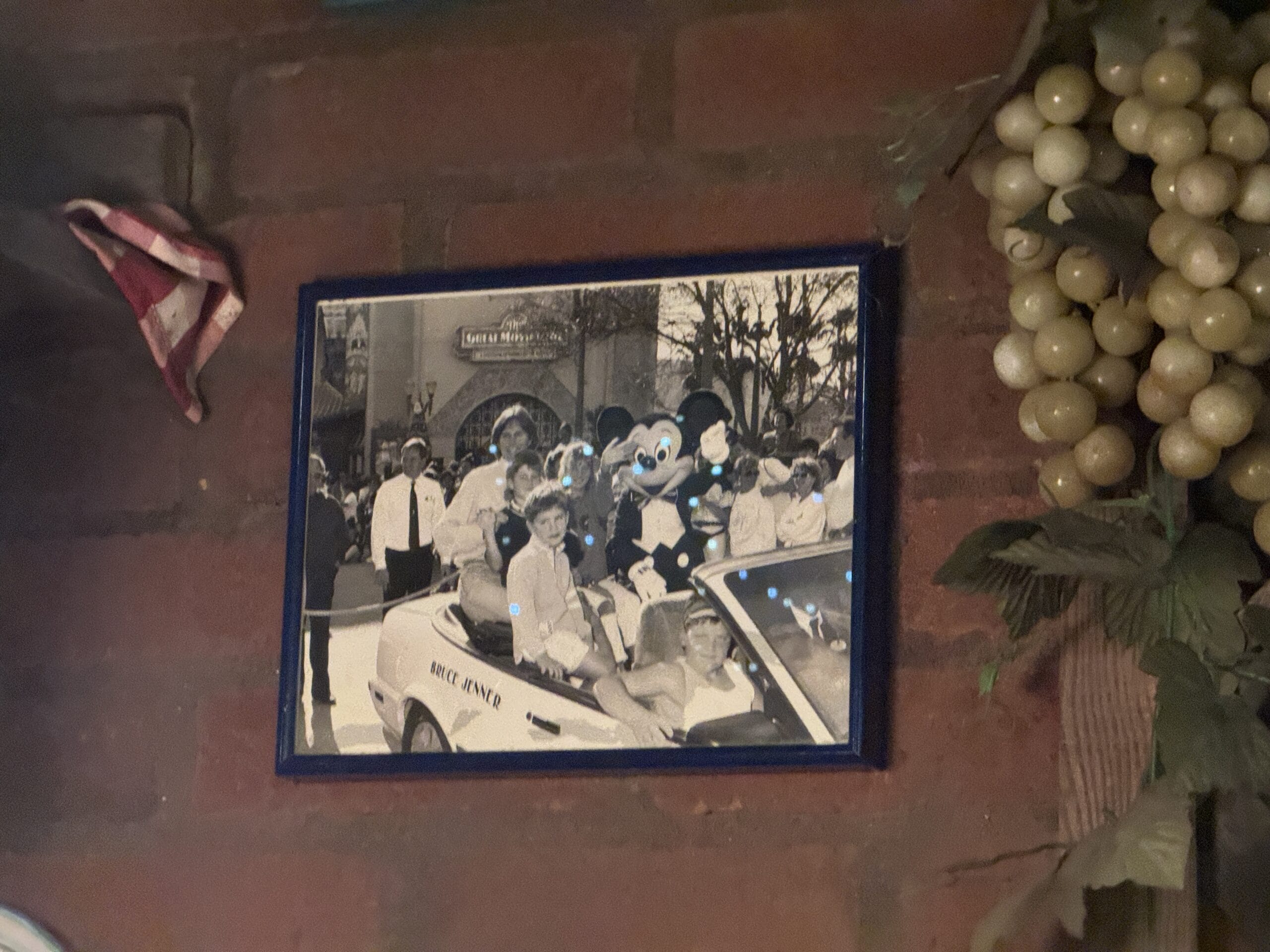 Framed black-and-white photo of people in a car with a mascot at Disney's Hollywood Studios, on a brick wall.