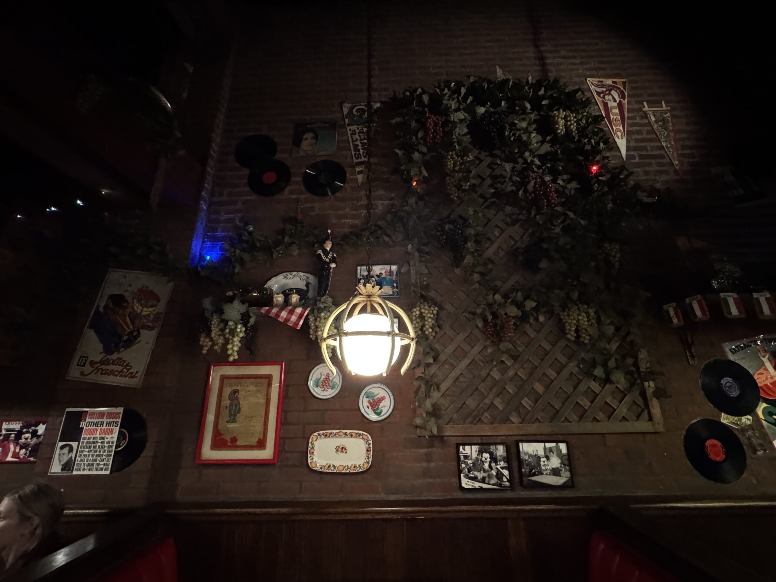 Dimly-lit wall at Mama Melrose’s Ristorante Italiano features vintage decor, hanging grapes, and nostalgic Disney's Hollywood Studios photos.