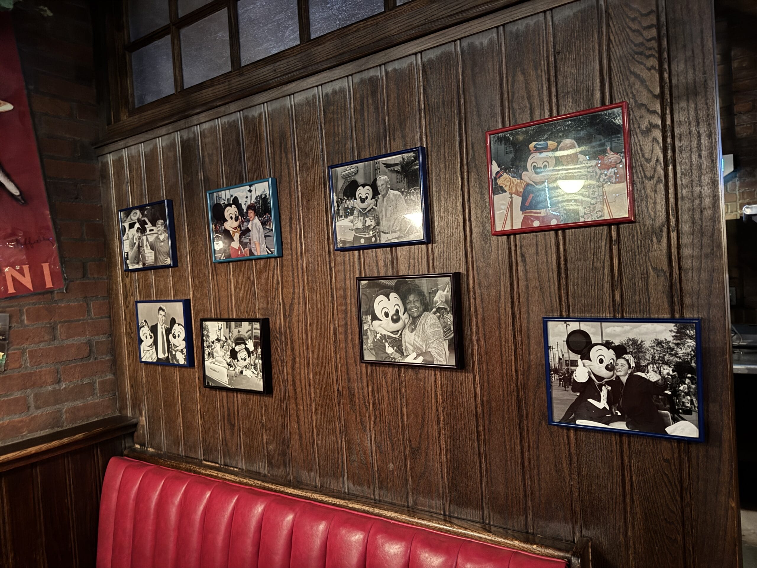 Framed photos of people with Mickey Mouse at Mama Melrose’s Ristorante Italiano hang above a red booth.