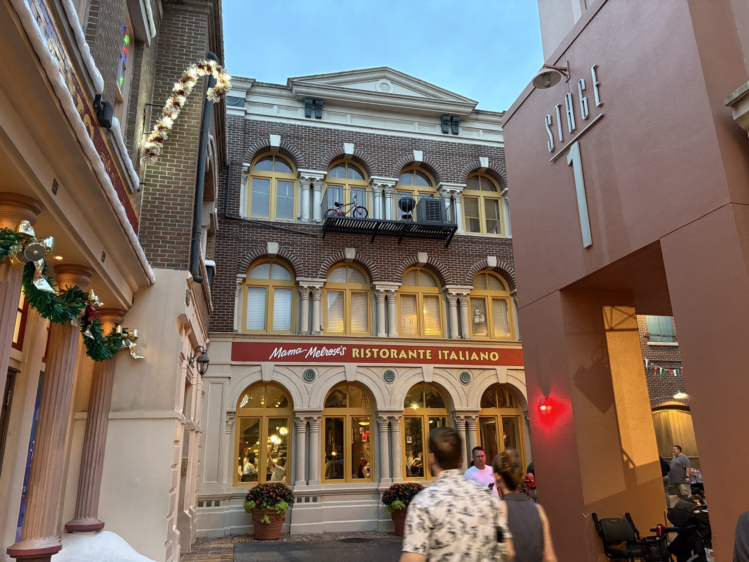Guests stroll by Mama Melrose’s Ristorante Italiano at Disney's Hollywood Studios, snapping photos of festive holiday décor.