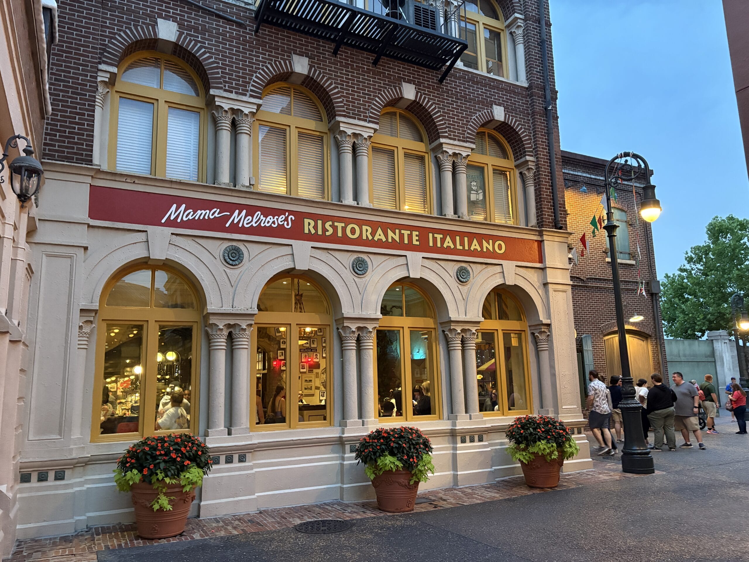 Guests snap photos outside Mama Melrose’s Ristorante Italiano at Disney's Hollywood Studios by arched windows and potted plants.