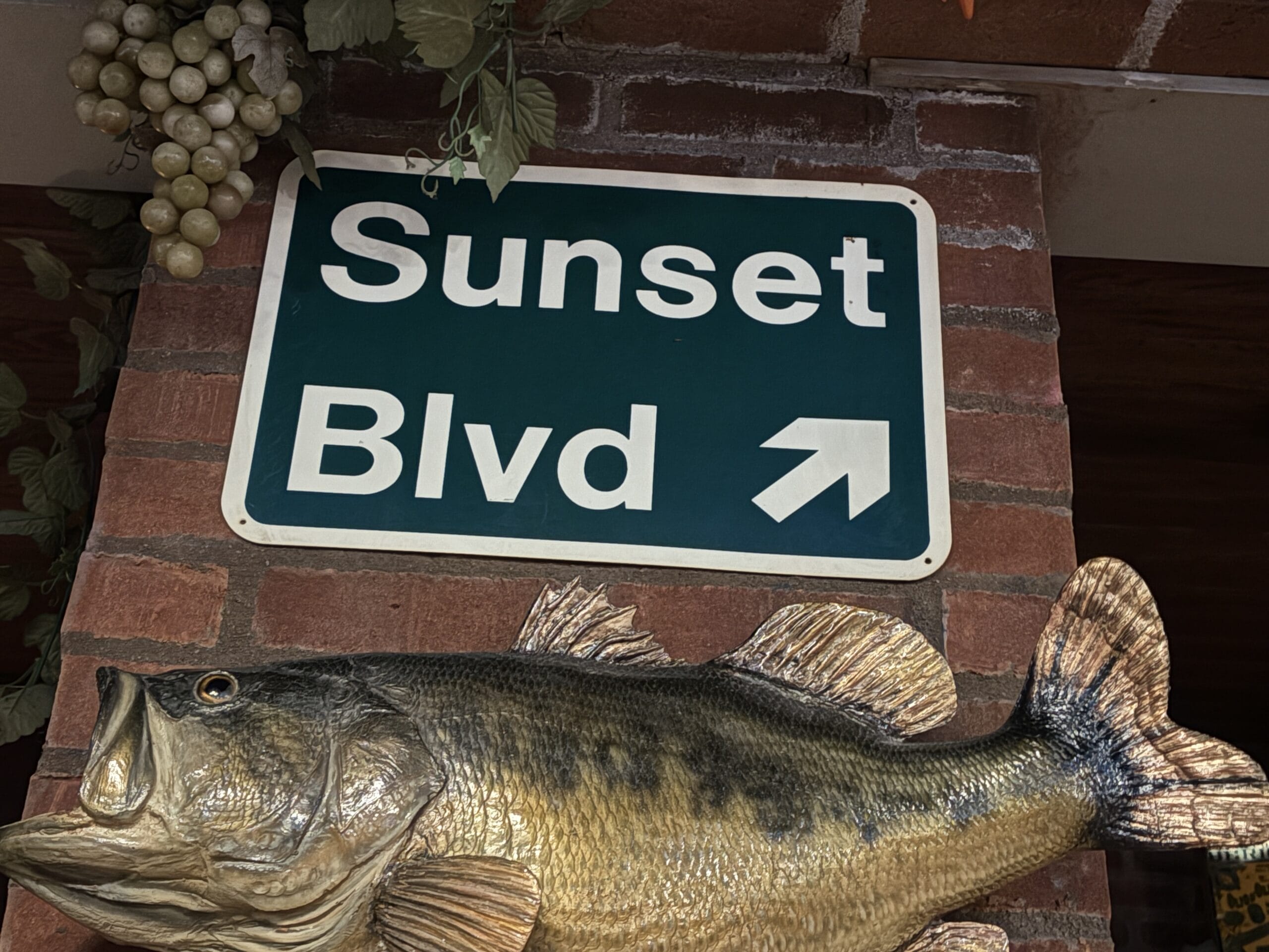 Photos of a green "Sunset Blvd" street sign at Mama Melrose’s Ristorante Italiano, mounted above a fish and fake grapes.