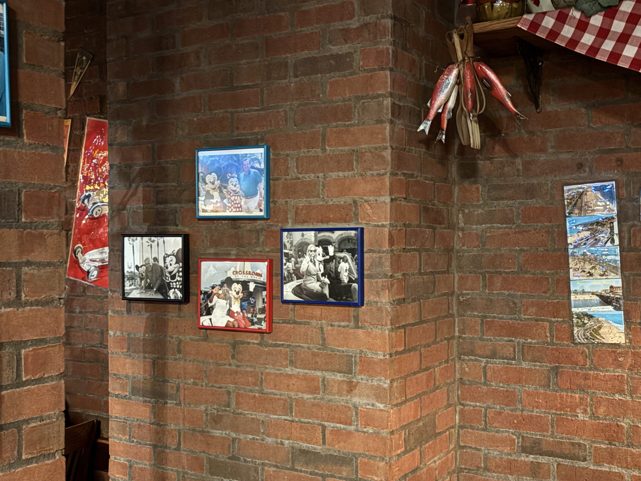 Framed photos and postcards hang on a red brick wall at Mama Melrose’s Ristorante Italiano in Disney's Hollywood Studios.
