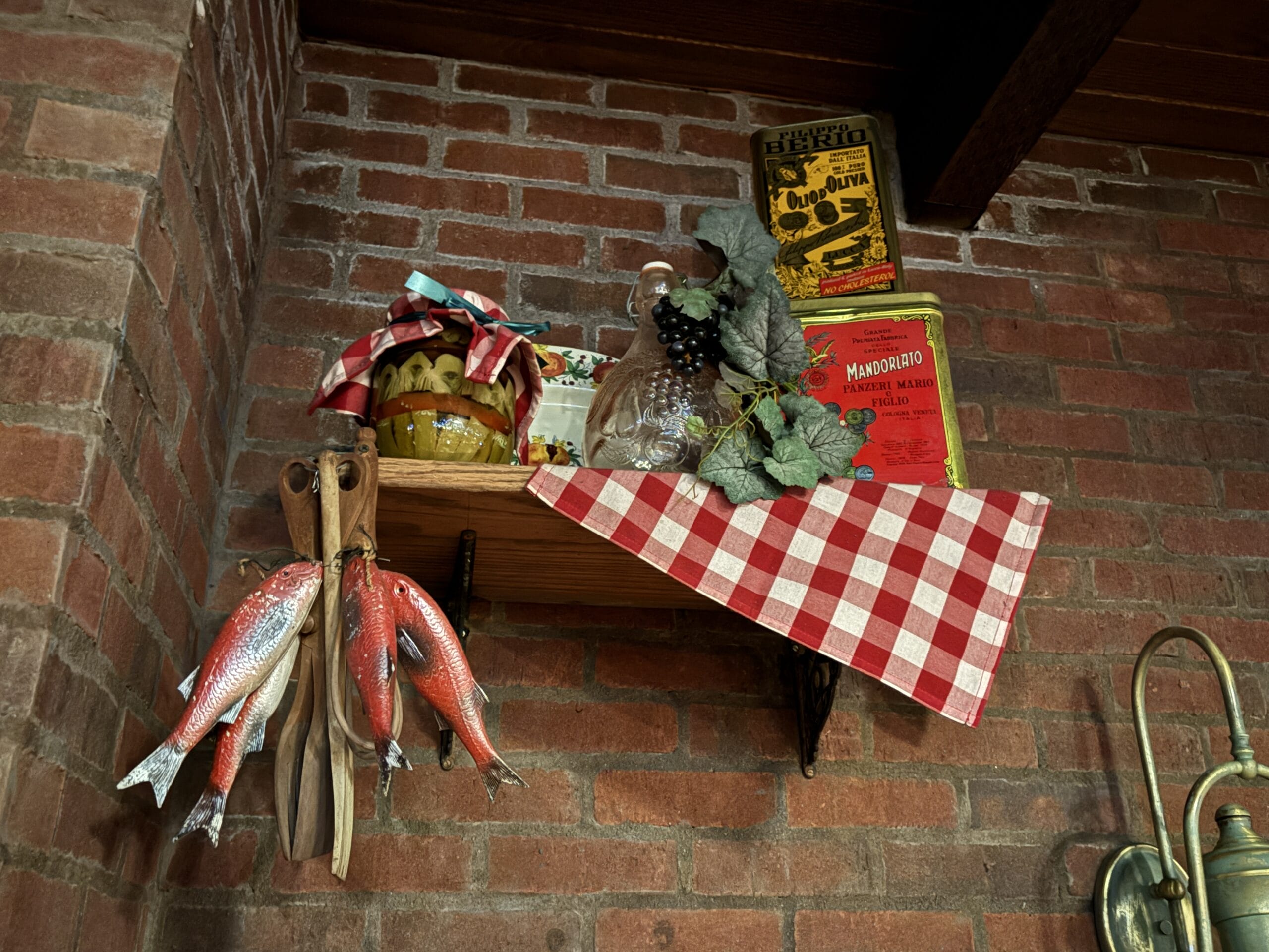 Wooden shelf on brick wall at Mama Melrose’s Ristorante Italiano with tins, grapes, and decor—perfect for PHOTOS.