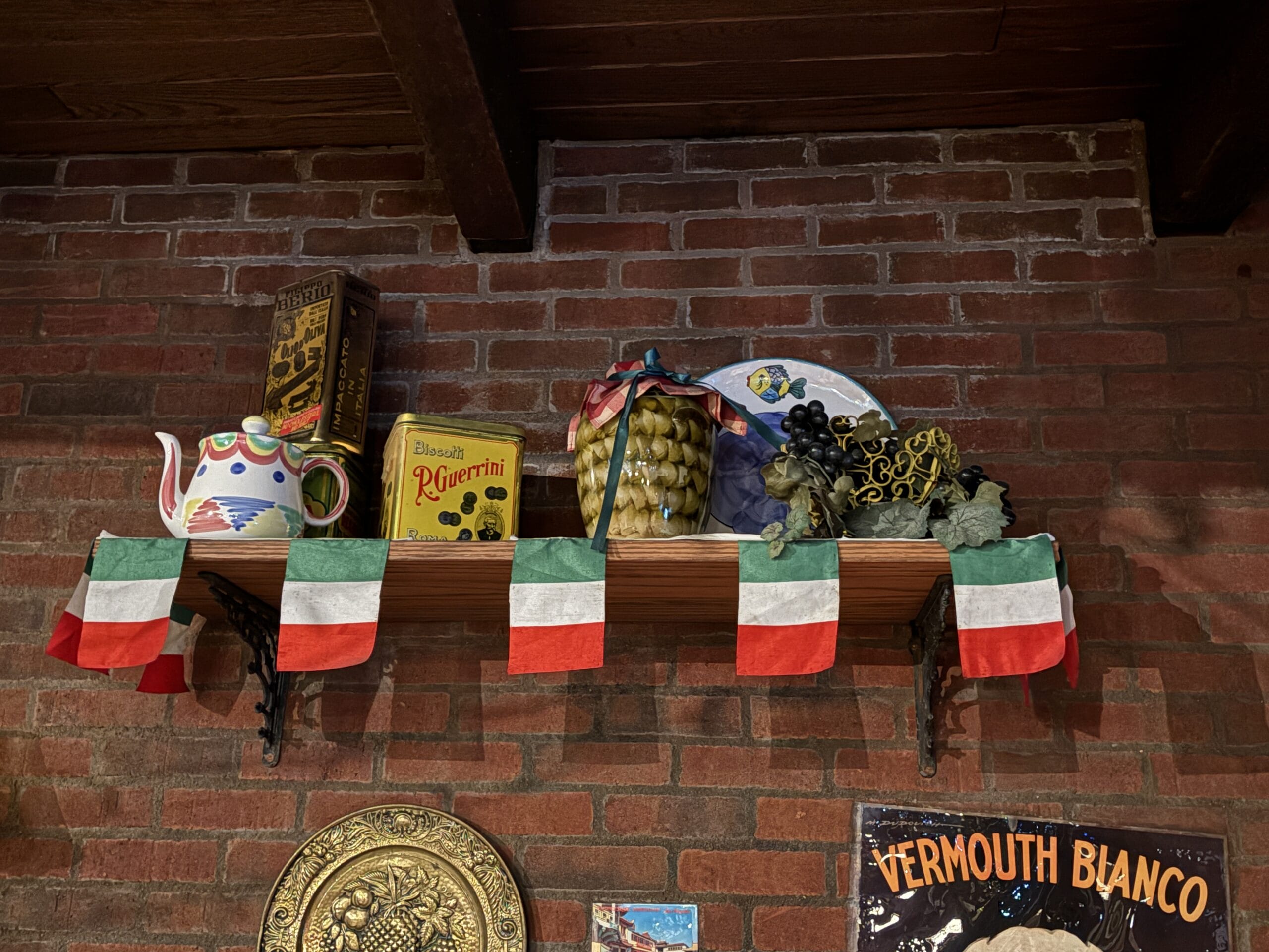A shelf at Mama Melrose’s Ristorante Italiano holds Italian decor, dishes, and a teapot above flag bunting—perfect for photos.
