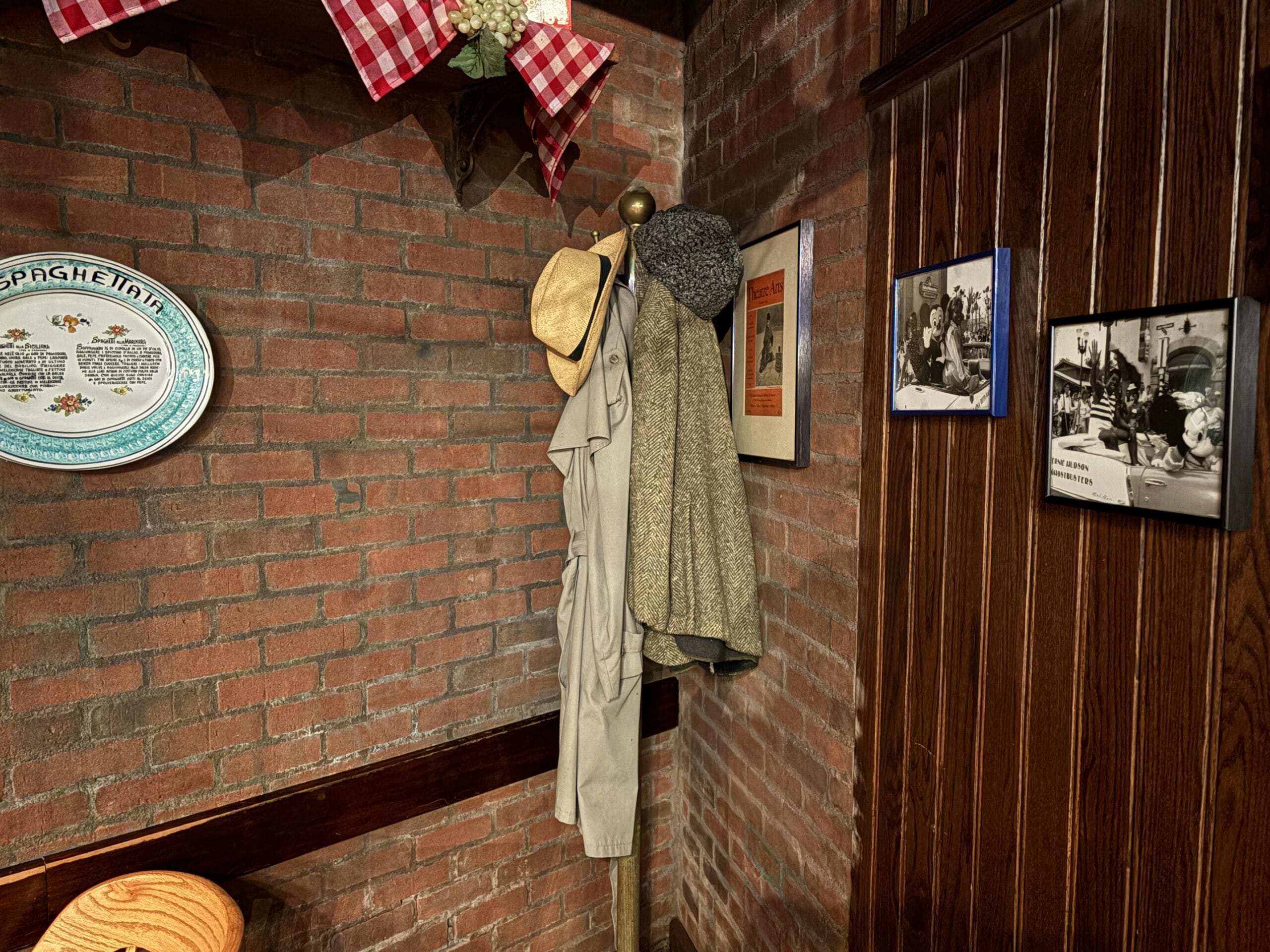 Coats and hats hang on a wooden rack by a brick wall with framed photos at Mama Melrose’s Ristorante Italiano.