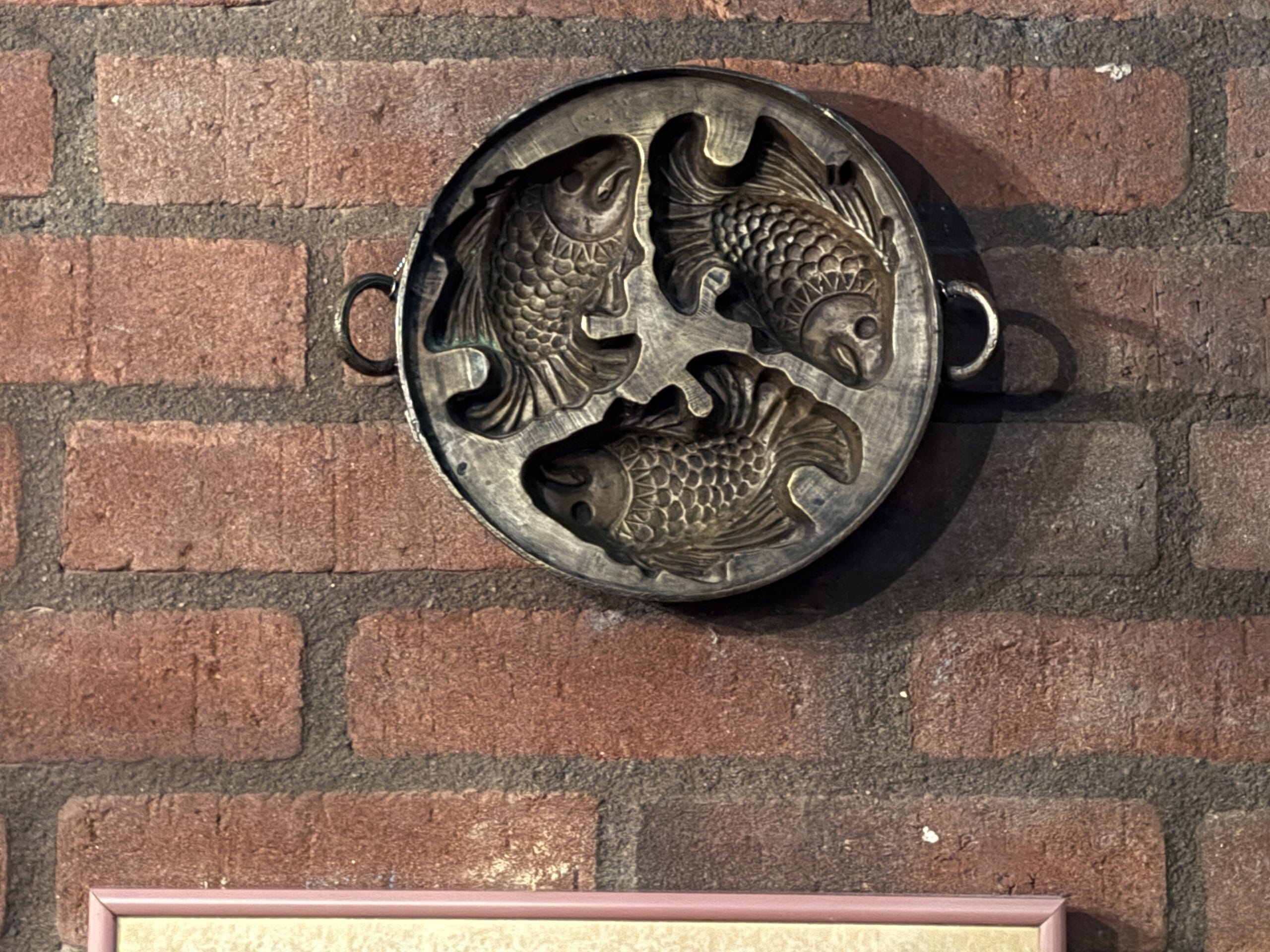 A round metal mold with three fish shapes hangs on a red brick wall at Mama Melrose’s Ristorante Italiano.